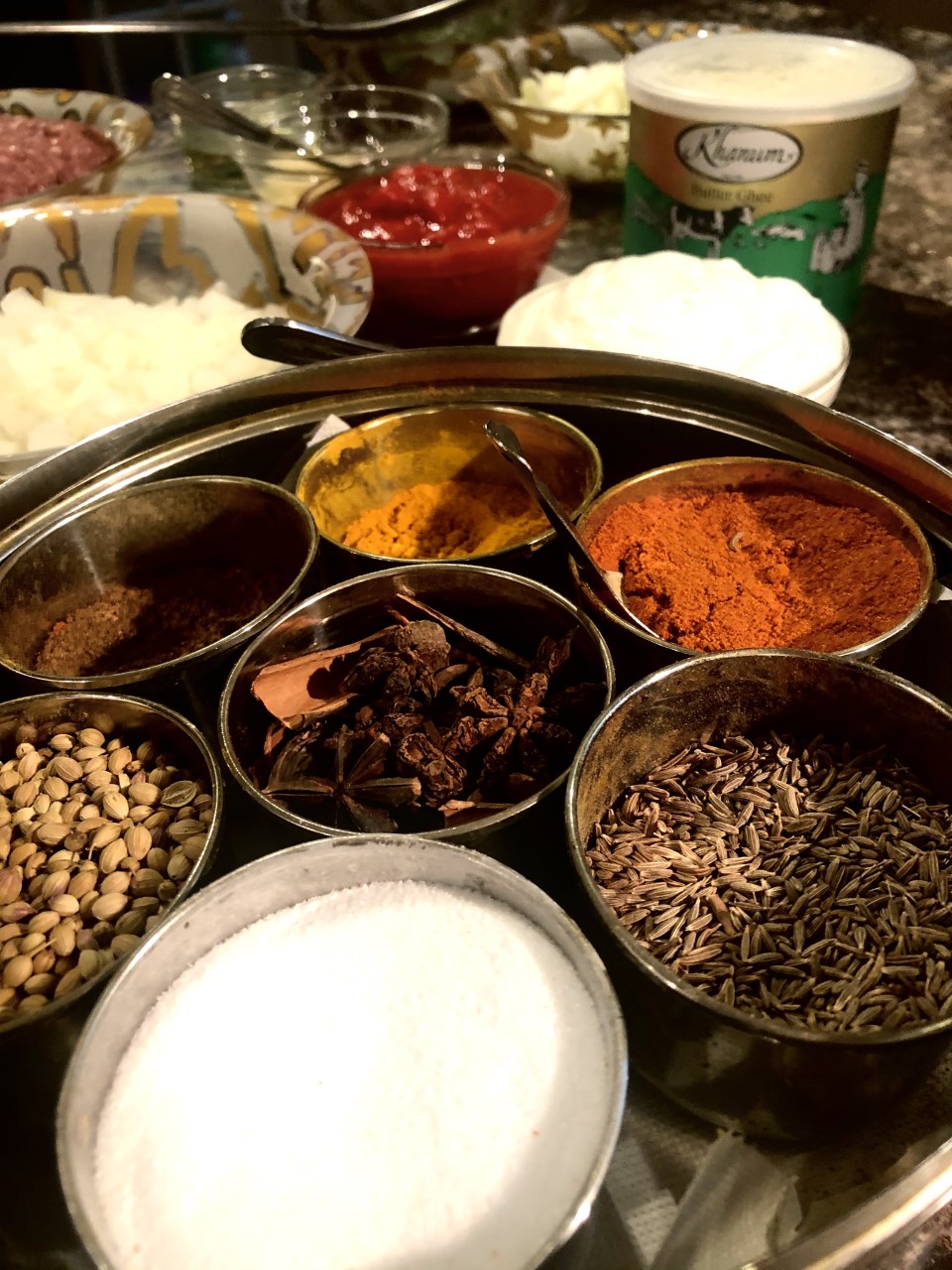A large tin with smaller pots in that all contain herbs. In the background you can see glass bowls with other ingredients like cream, mince and tomatoes.