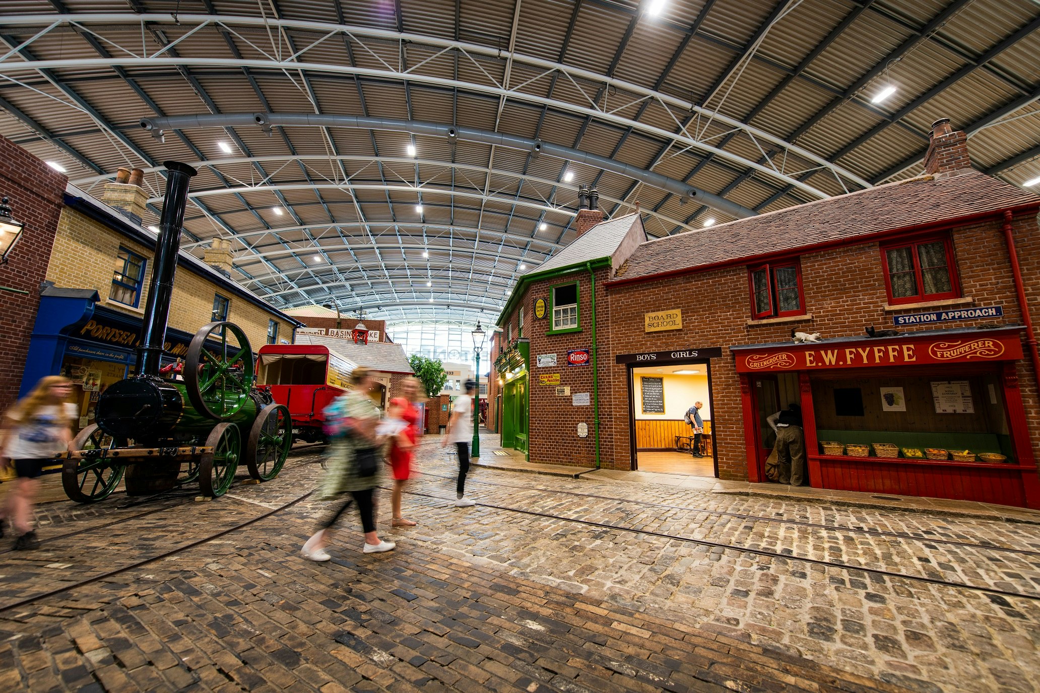 The cobbled streets of milestones museum. You can see some shops and vehicles and people walking around.