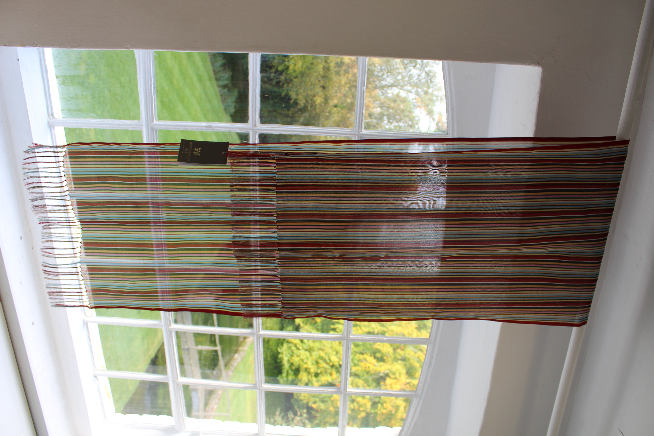 A colourful stripy silk scarf hanging from a curtain pole