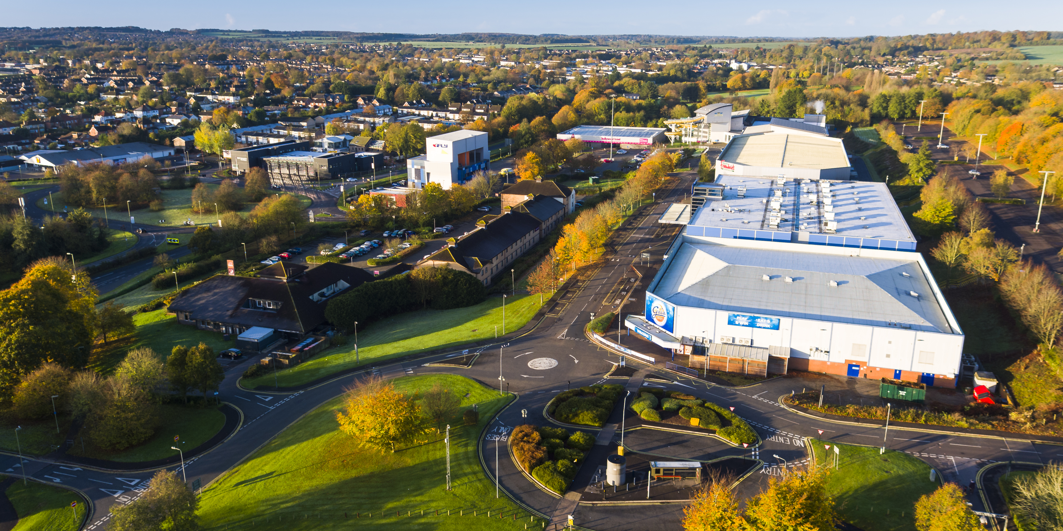 You can see a number of large white buildings from the air which are on the Leisure Park. You can see a roundabout and the road. Then lots of trees.