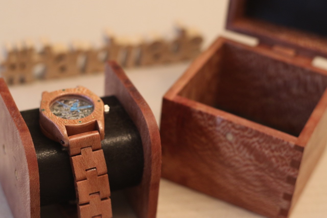 A wooden watch sat in a holder which goes into a wooden box.