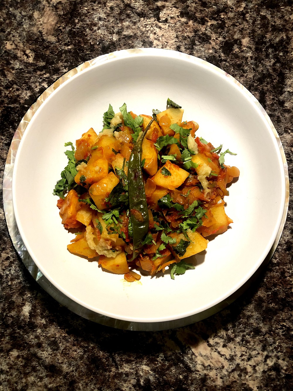 A white plate on a marble worktop. It has a potato, tomato and greens dish in it.