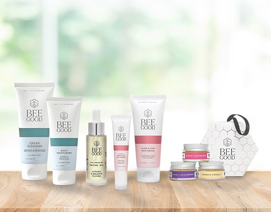 A selection of cosmetics tubes and pots with a bee good box. they all sit on a wooden top.