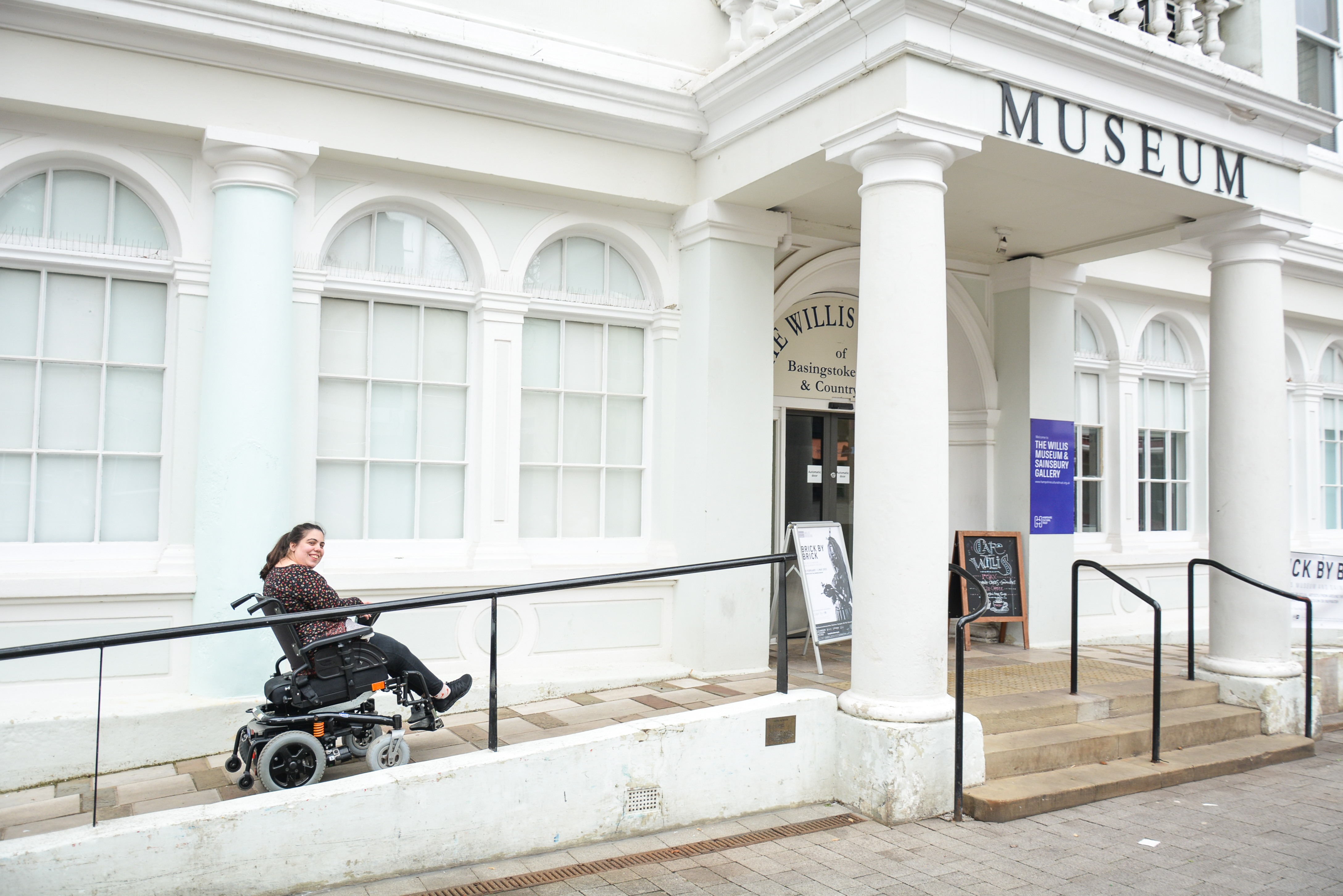 A lady sits in a wheelchair and is going up the slope towards the Willis Museum