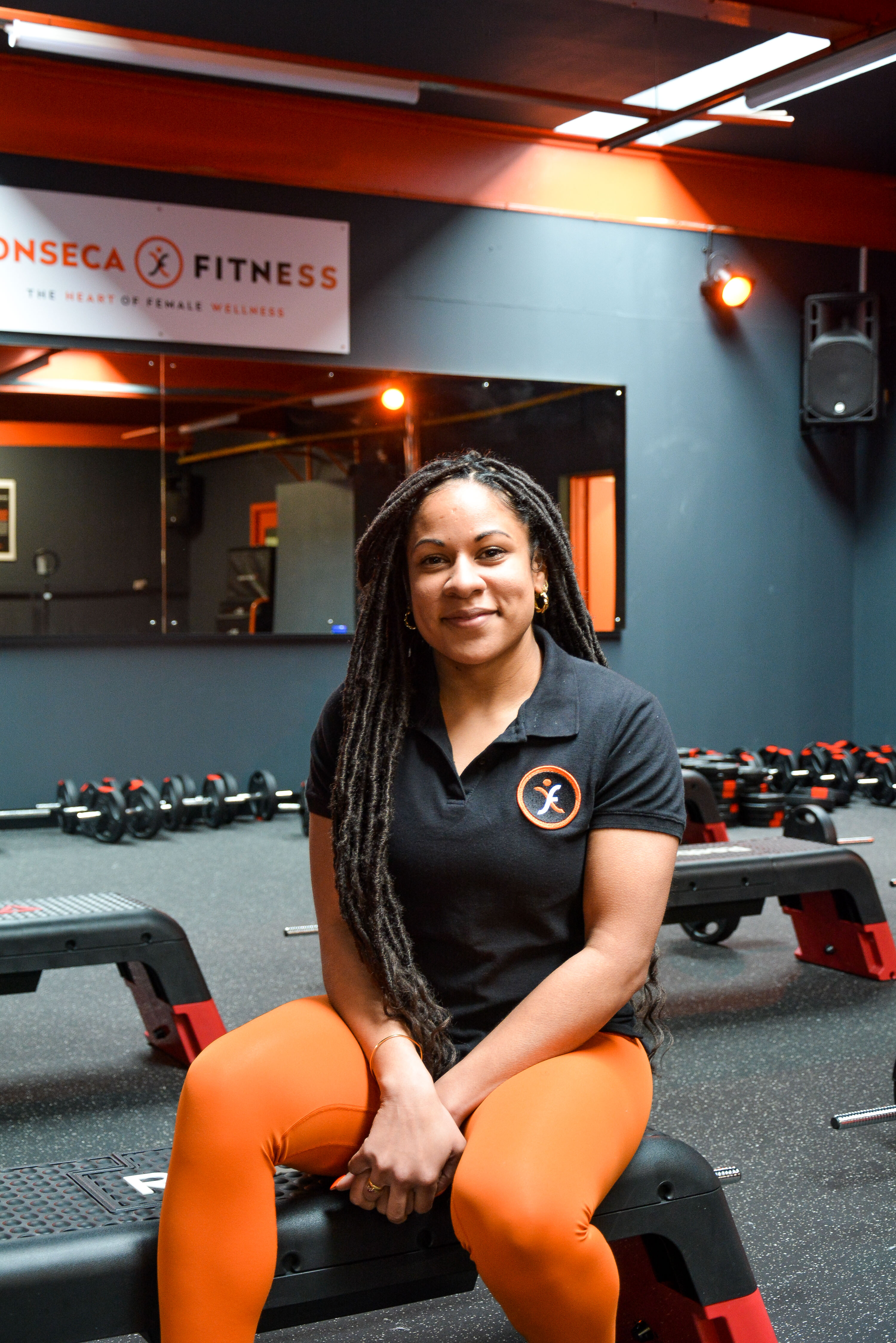 A female sits on a step looking at the camera. She wears a black t shirt and orange leggings