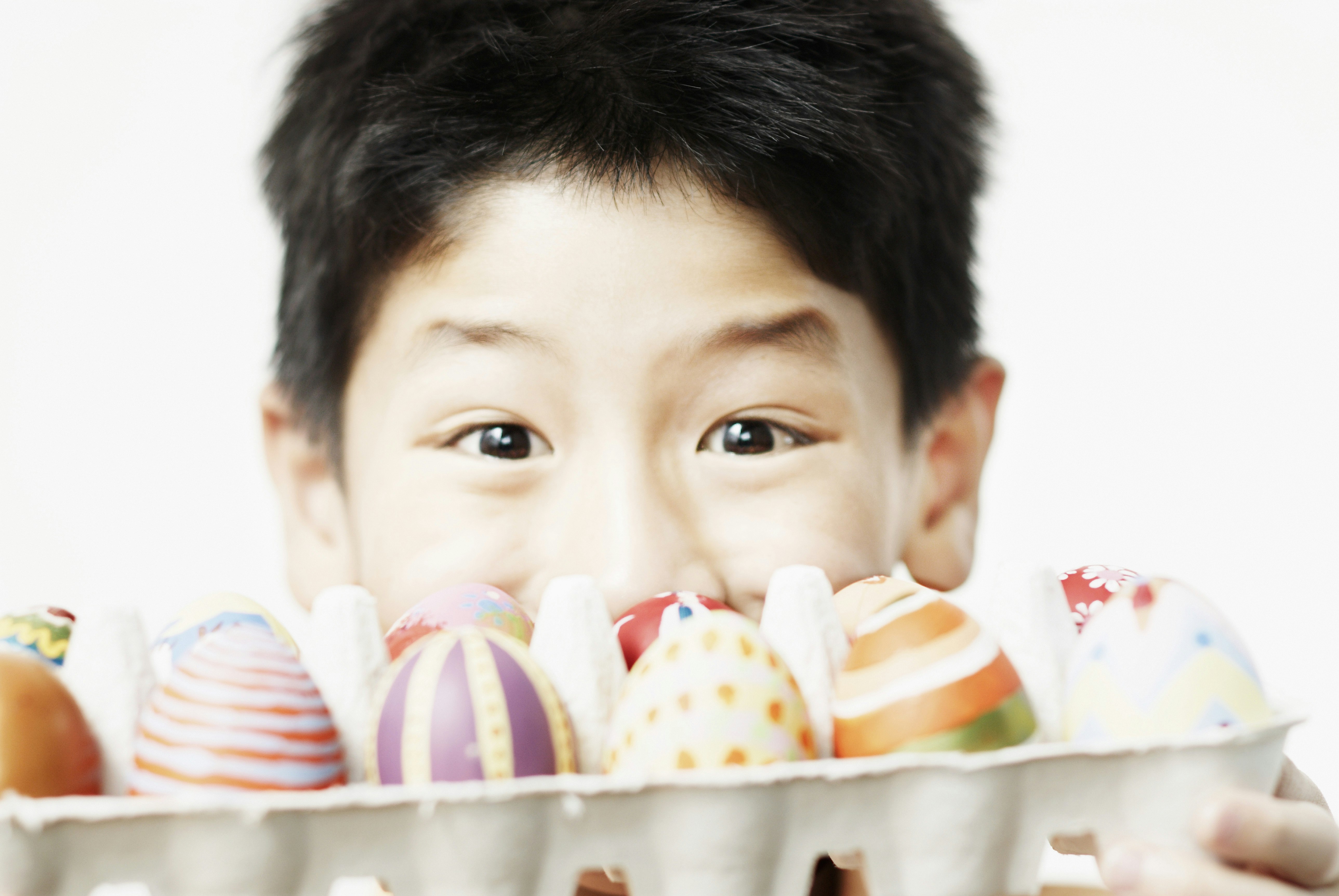 A boy looks at the camera and is half covered by a box of handpainted eggs.
