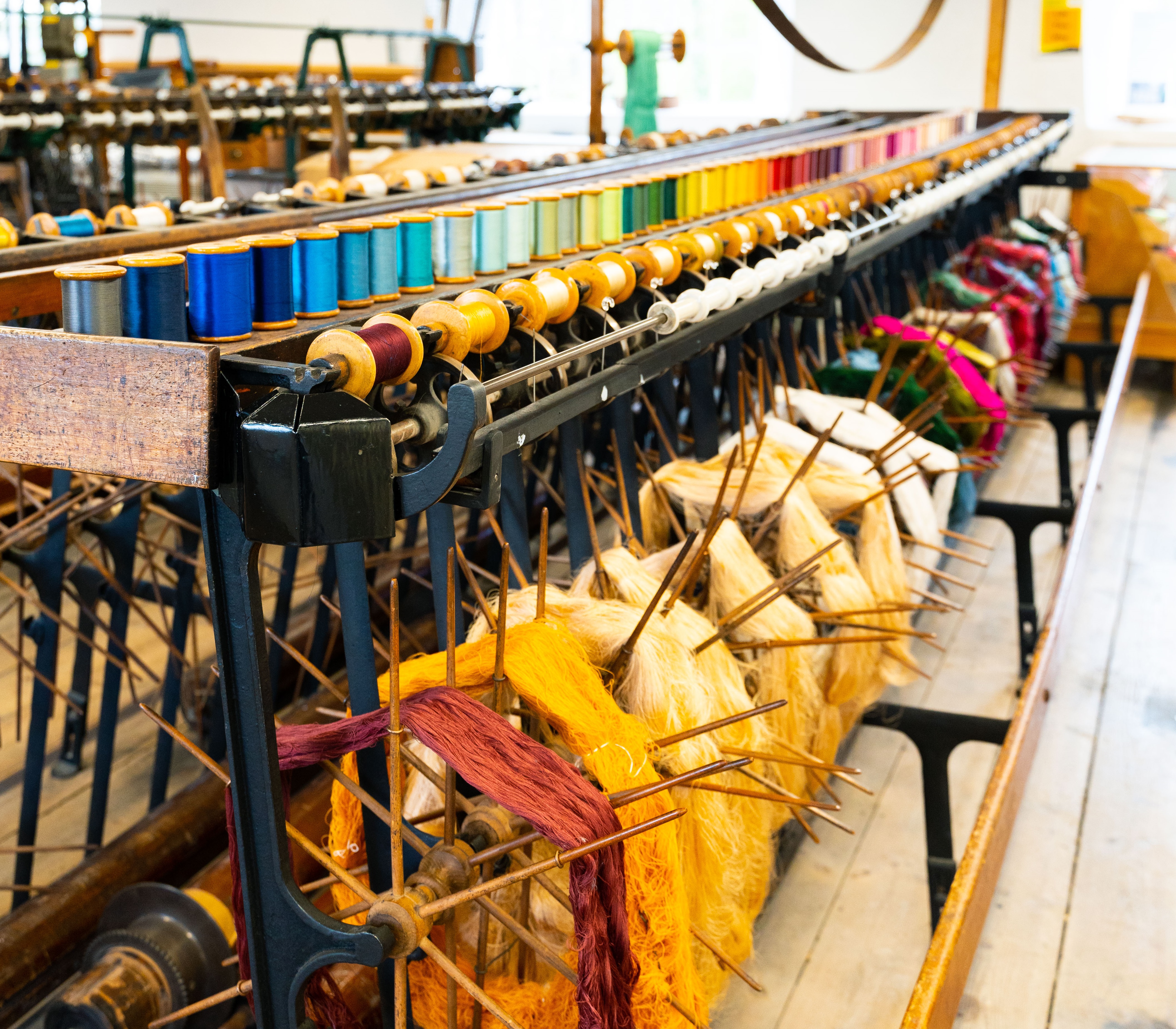 Image shows vintage machinery within a Silk Mill museum. Colourful threads in a rainbow of colours line the loom.