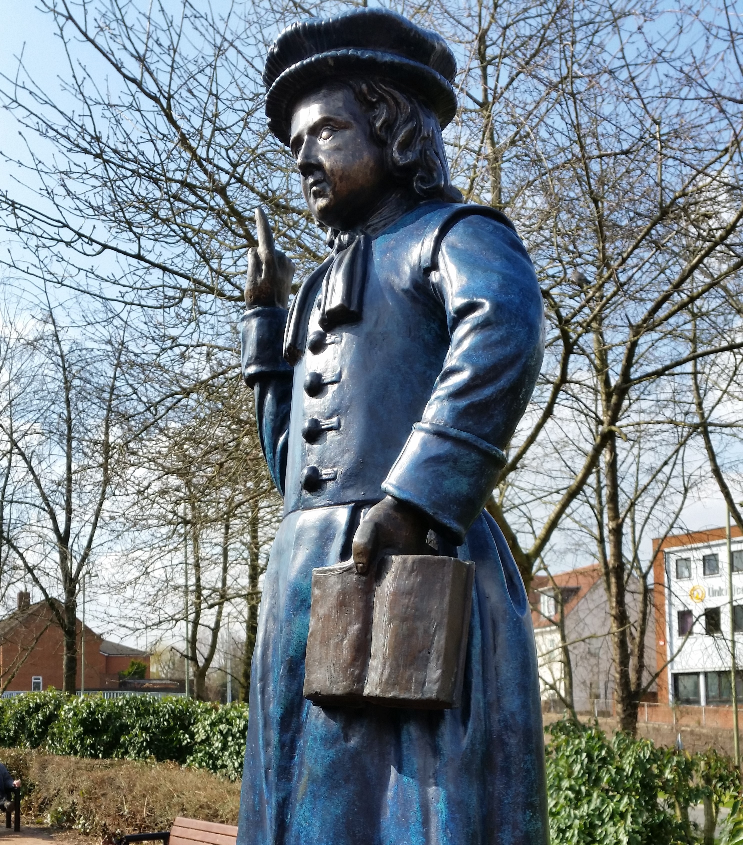 A blue statue stands on a brick plinth. The statue is a young boy dressed in a school uniform.