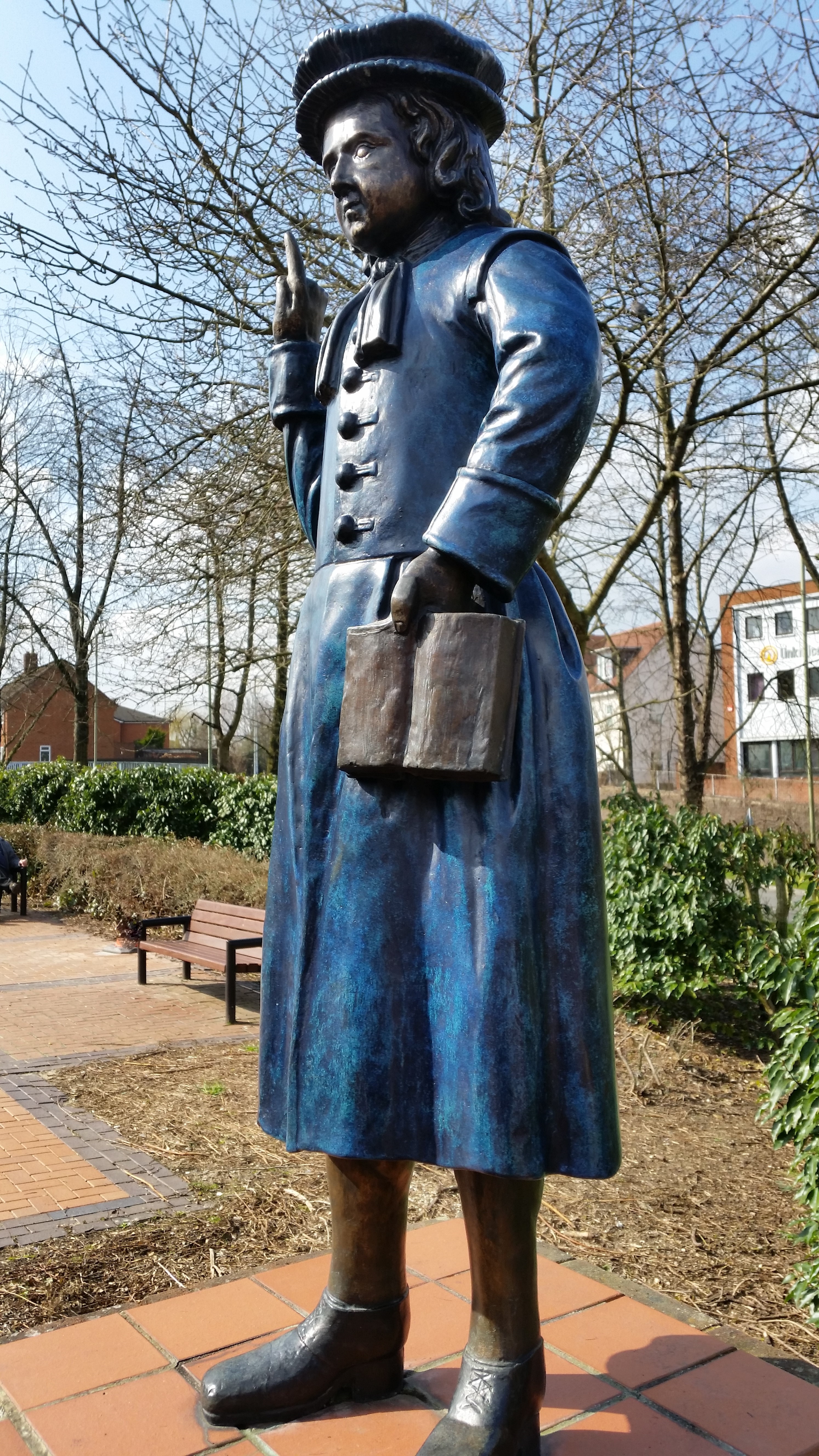 A blue statue stands on a brick plinth. The statue is a young boy dressed in a school uniform.