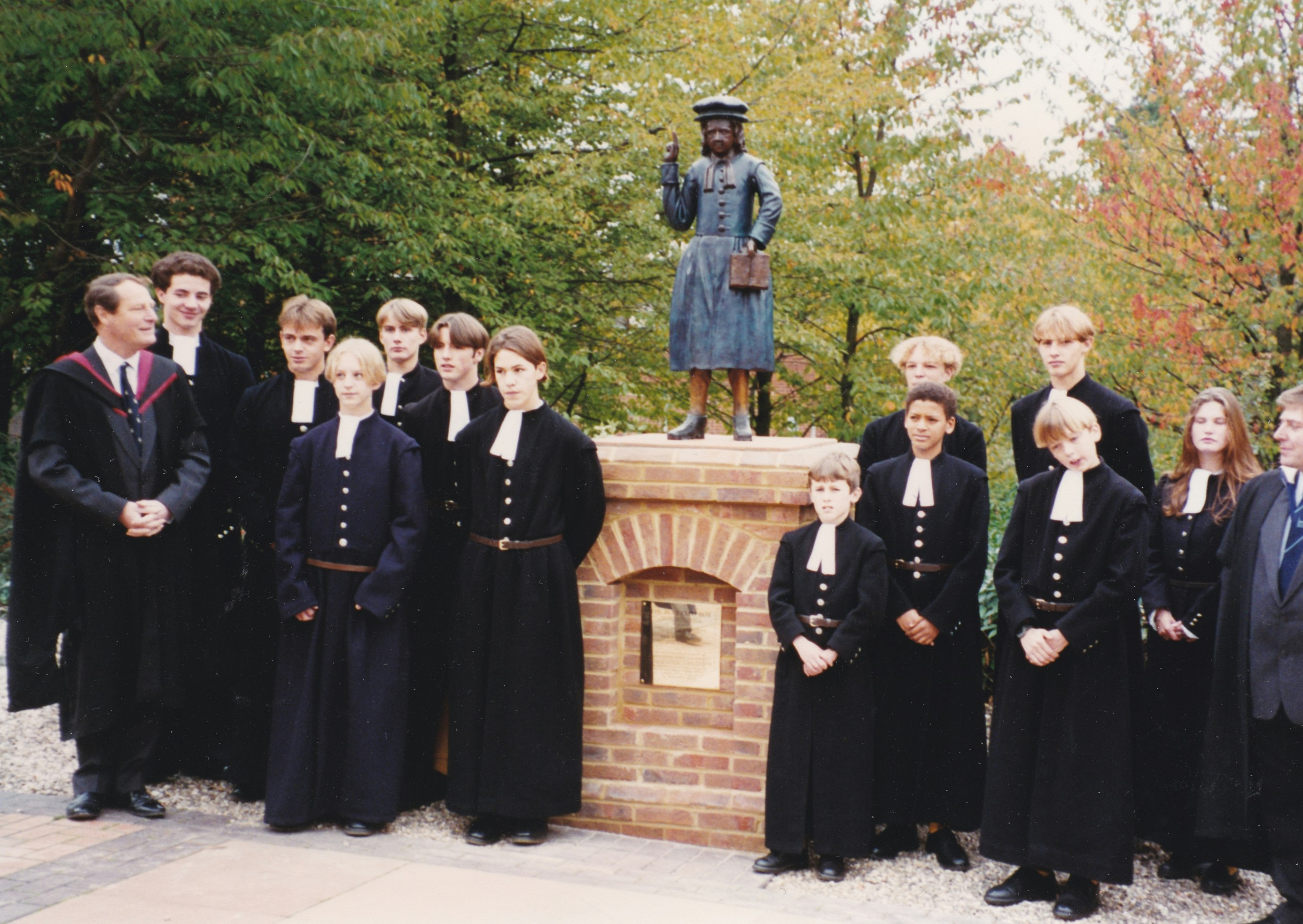 A group of pupils and teachers wearing a black and white uniform stand outside the Blue Coat Boy statue.