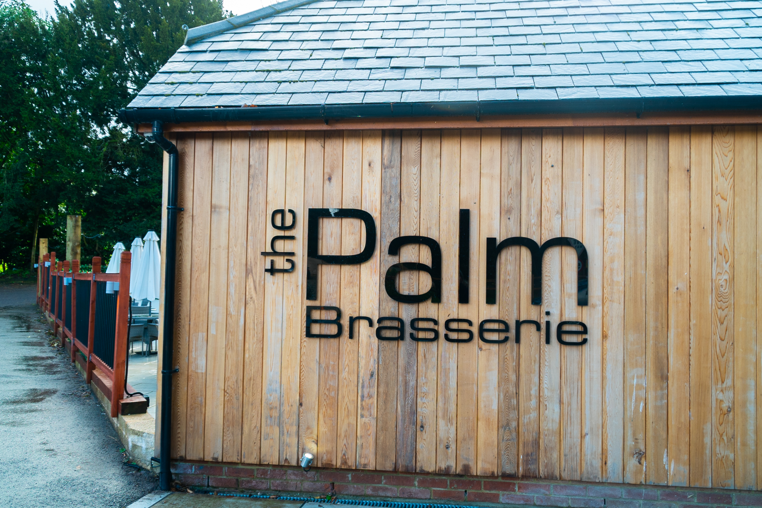 The outside of the building. A wooden slatted building with grey slate roof.