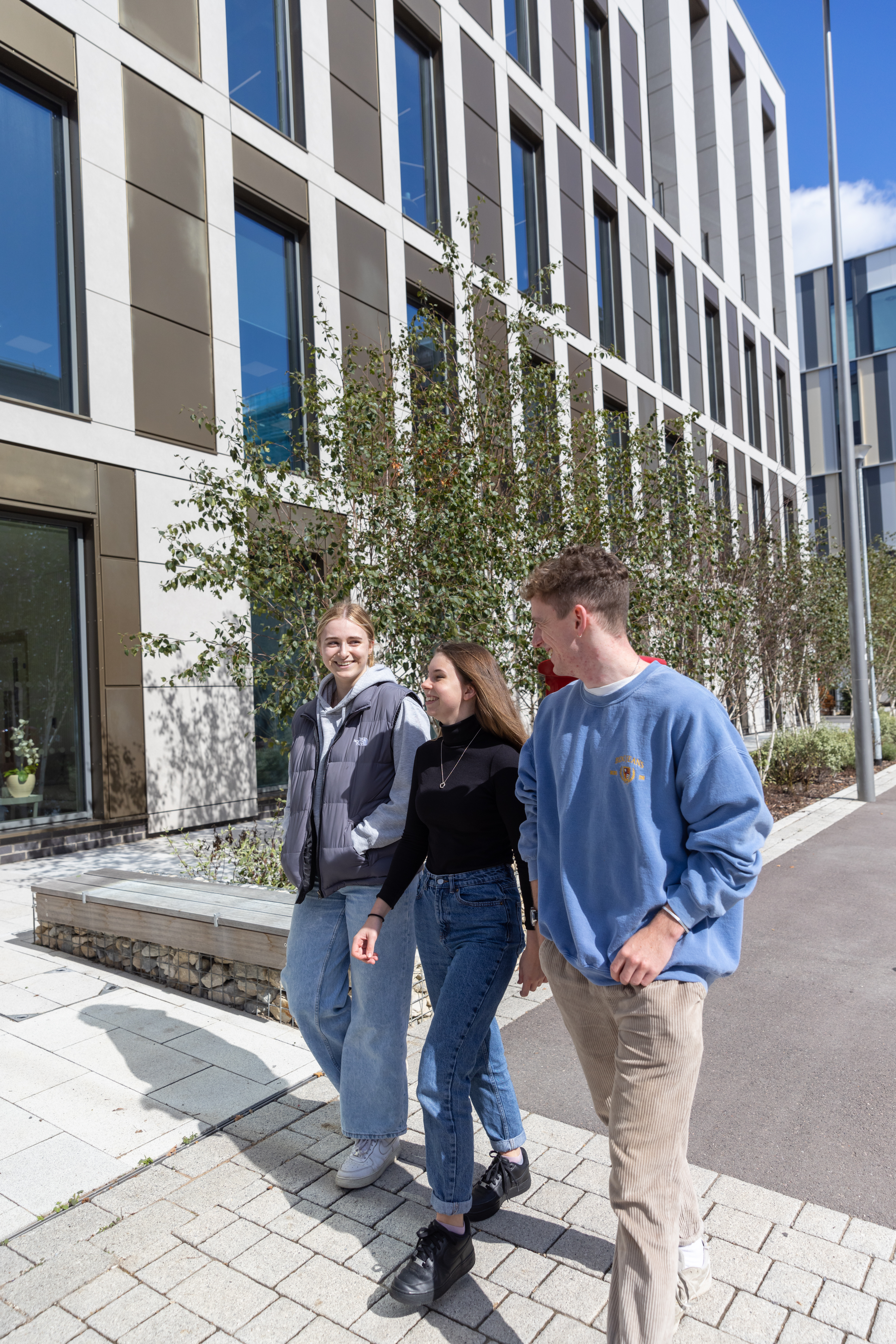 A group of young people walking along the street. You can see a modern building in the background.