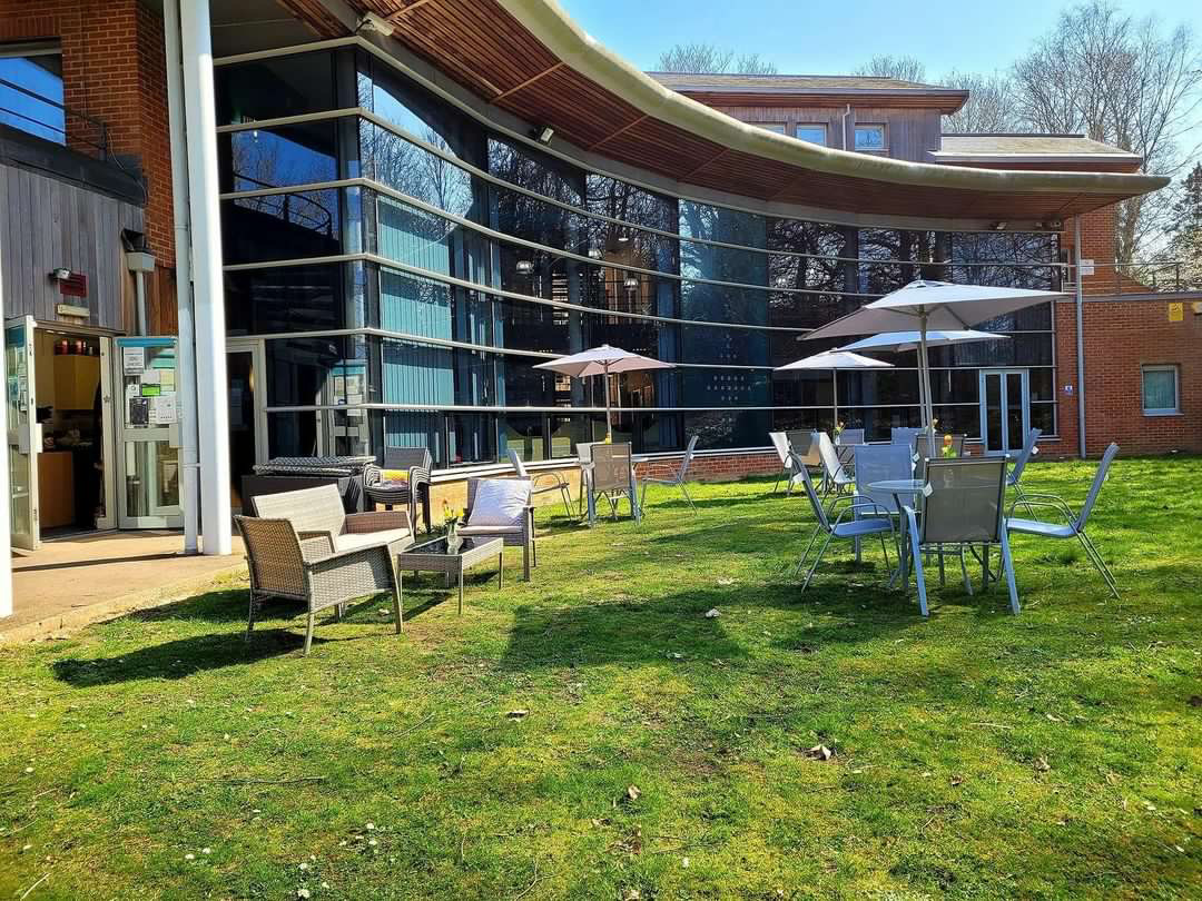 A curved glass and red brick building. It has tables and chairs outside.