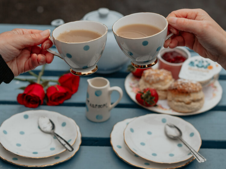 Two cups of tea are held with scones in the background
