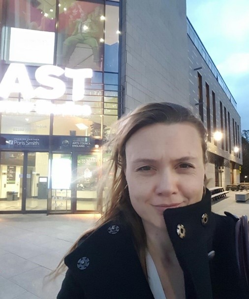 A lady stands in front of a building looking at the camera