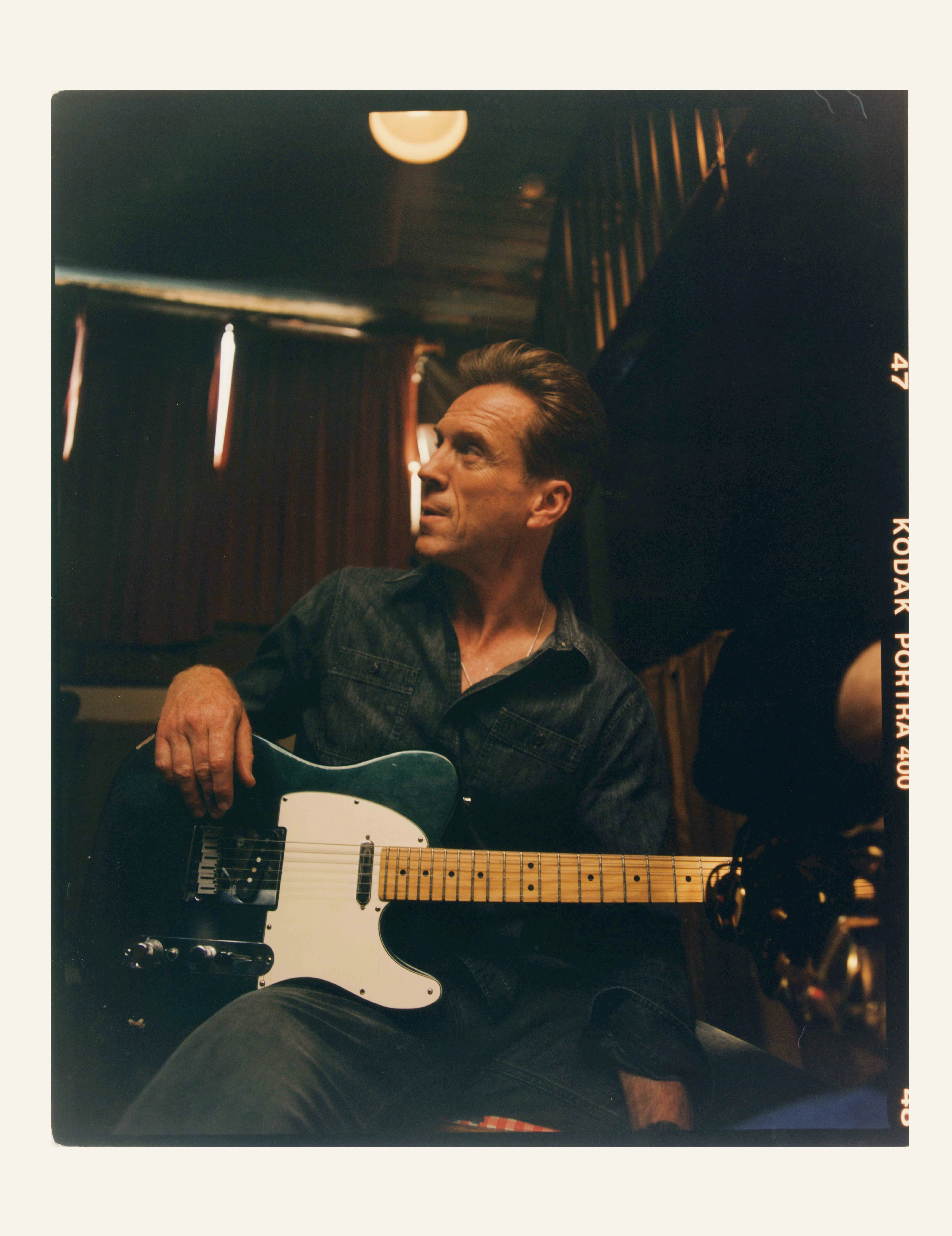 A man sits with an electric guitar on his lap