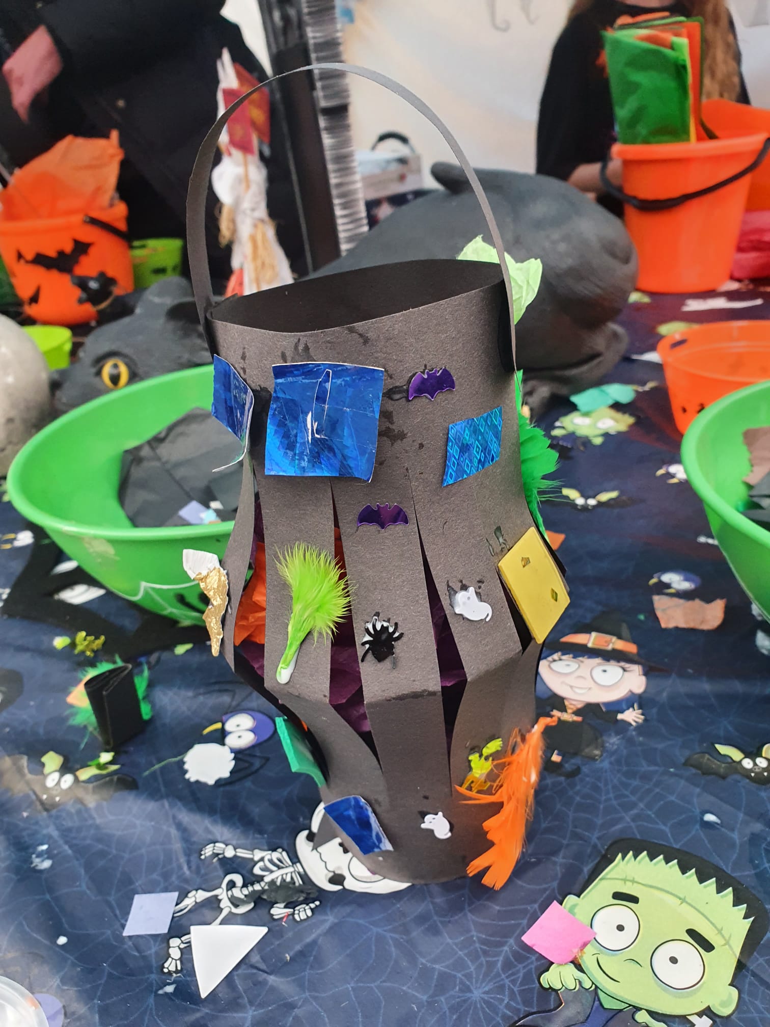 A black card lantern decorated with feathers and coloured paper.