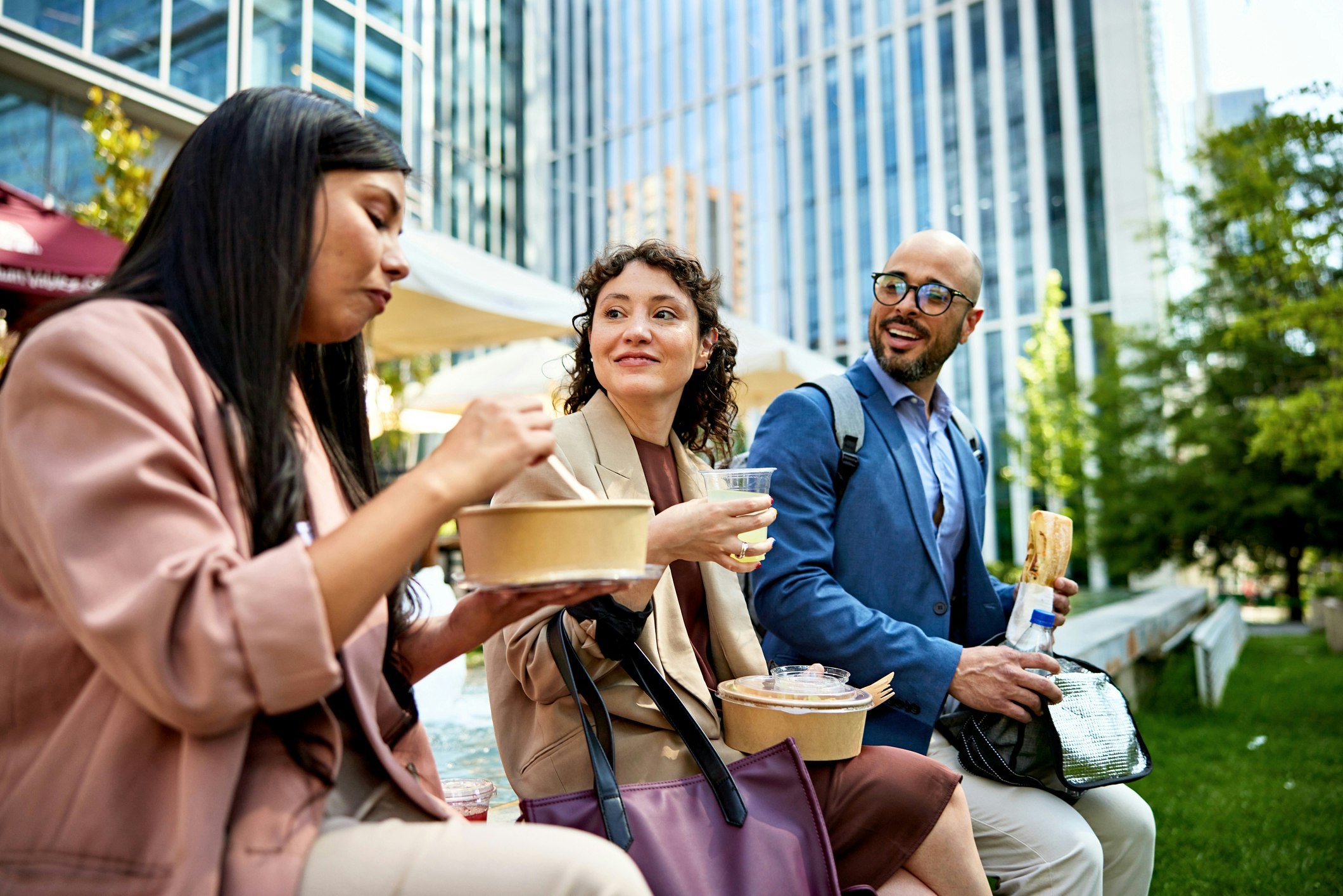 Three people sit eating their lunch and are outside.