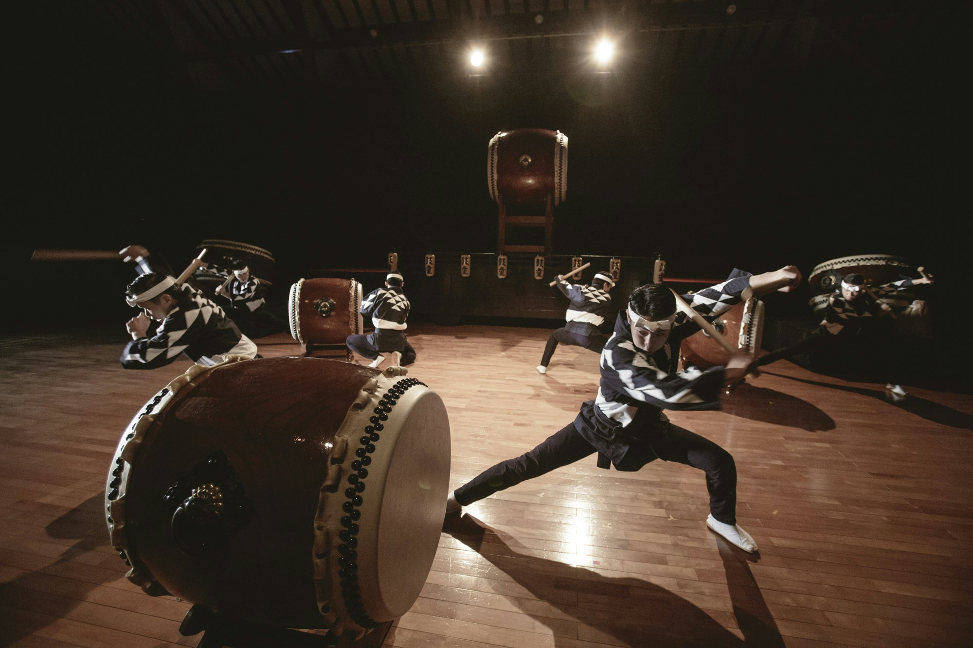 A group of Japanese drum players play on a stage. They wear black and white outfits.