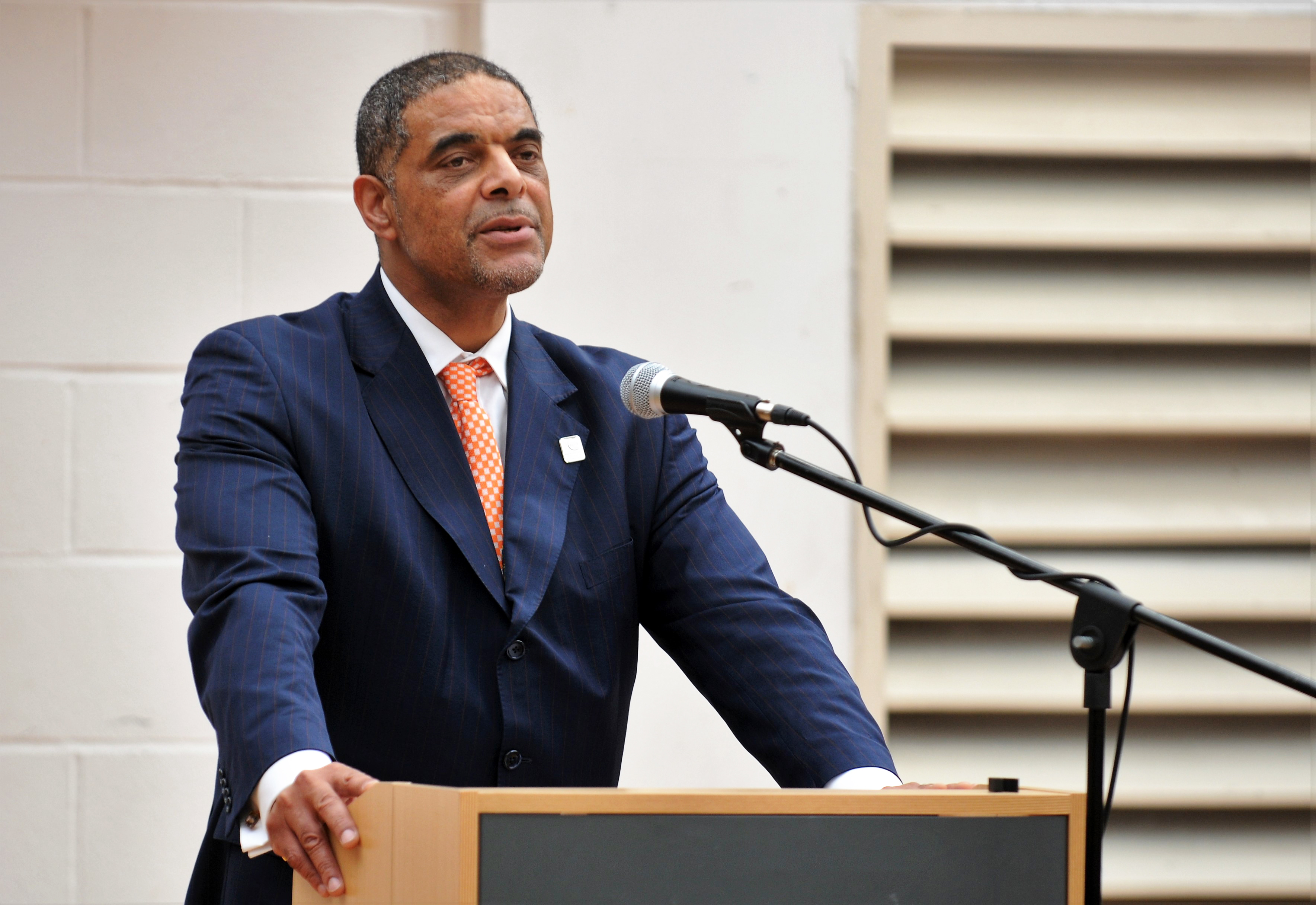 Anthony Bravo of Basingstoke College of Technology wears a blue suit and stands behind a lecturn and microphone.