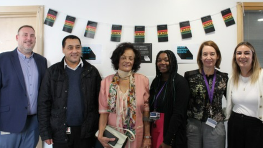 A group of five people stand together smiling at the camera. They are grouped together to celebrate the unveiling a plaque for mama Jean in honour of her trailblazing contribution to shaping the healthcare system in Basingstoke and nursing training.