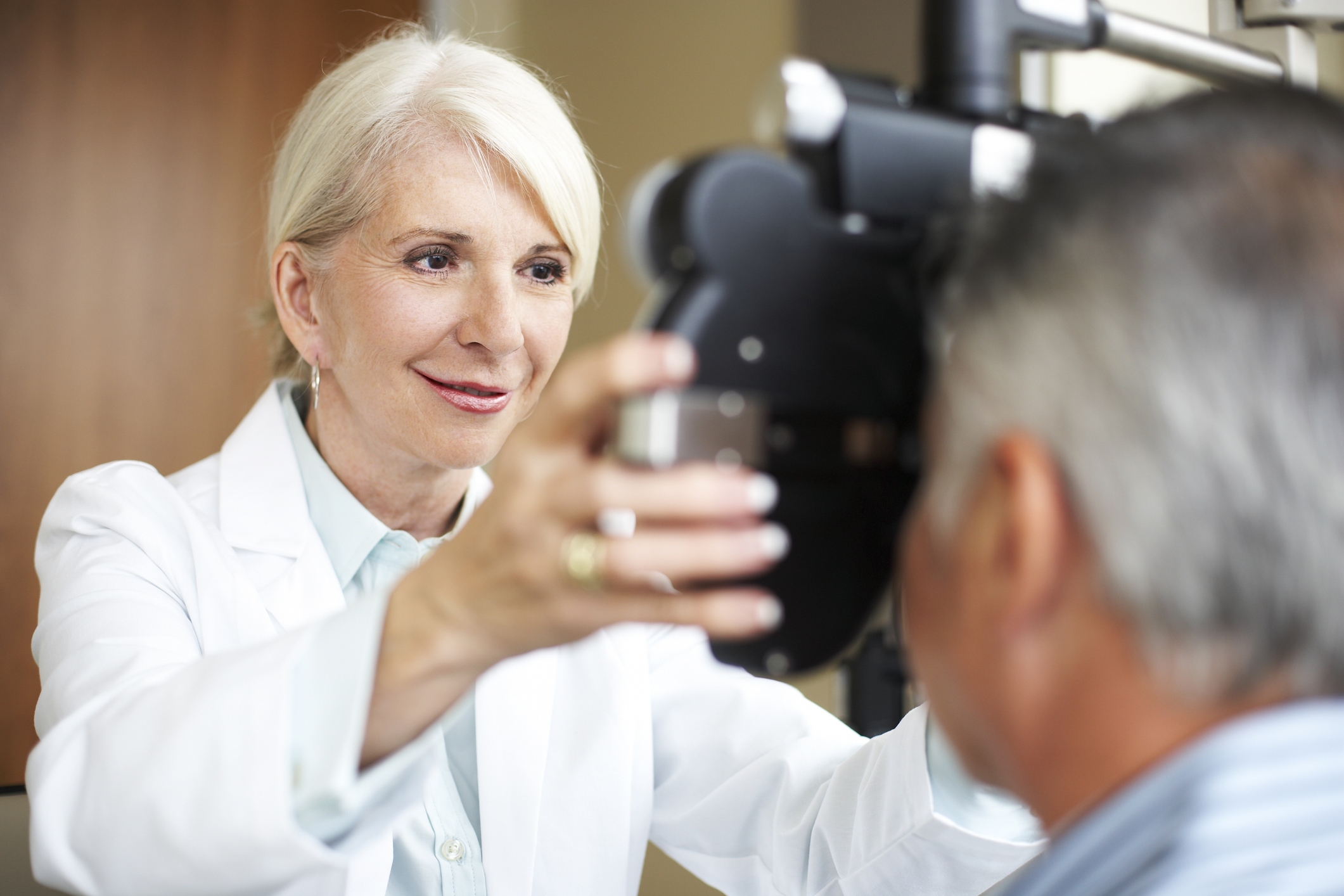 An optician holds a piece of equipment up to a patients eyes. The patient looks away from the camera.