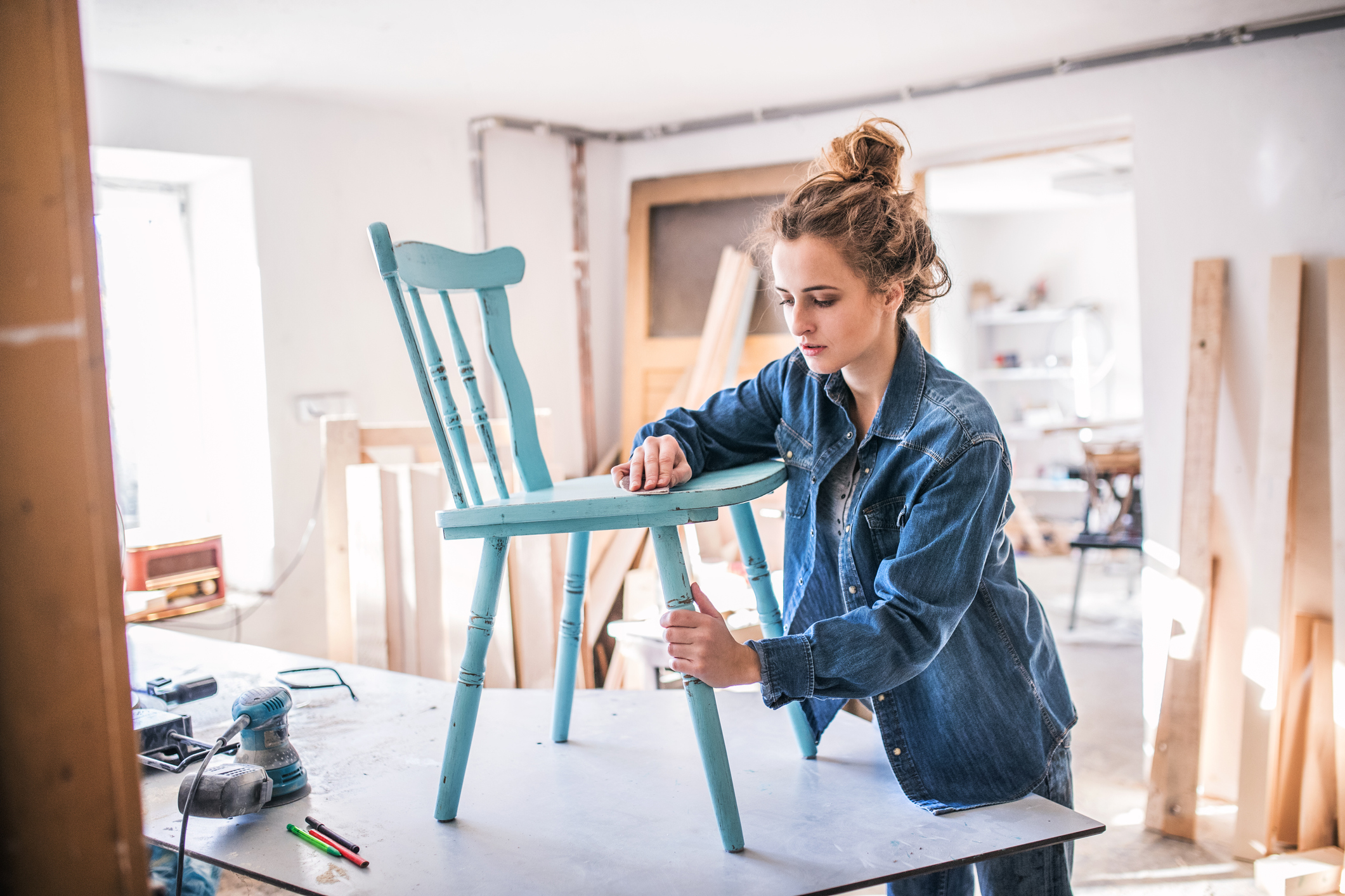 A person stands beside a wooden chair, the person seems to be upcycling the chair.