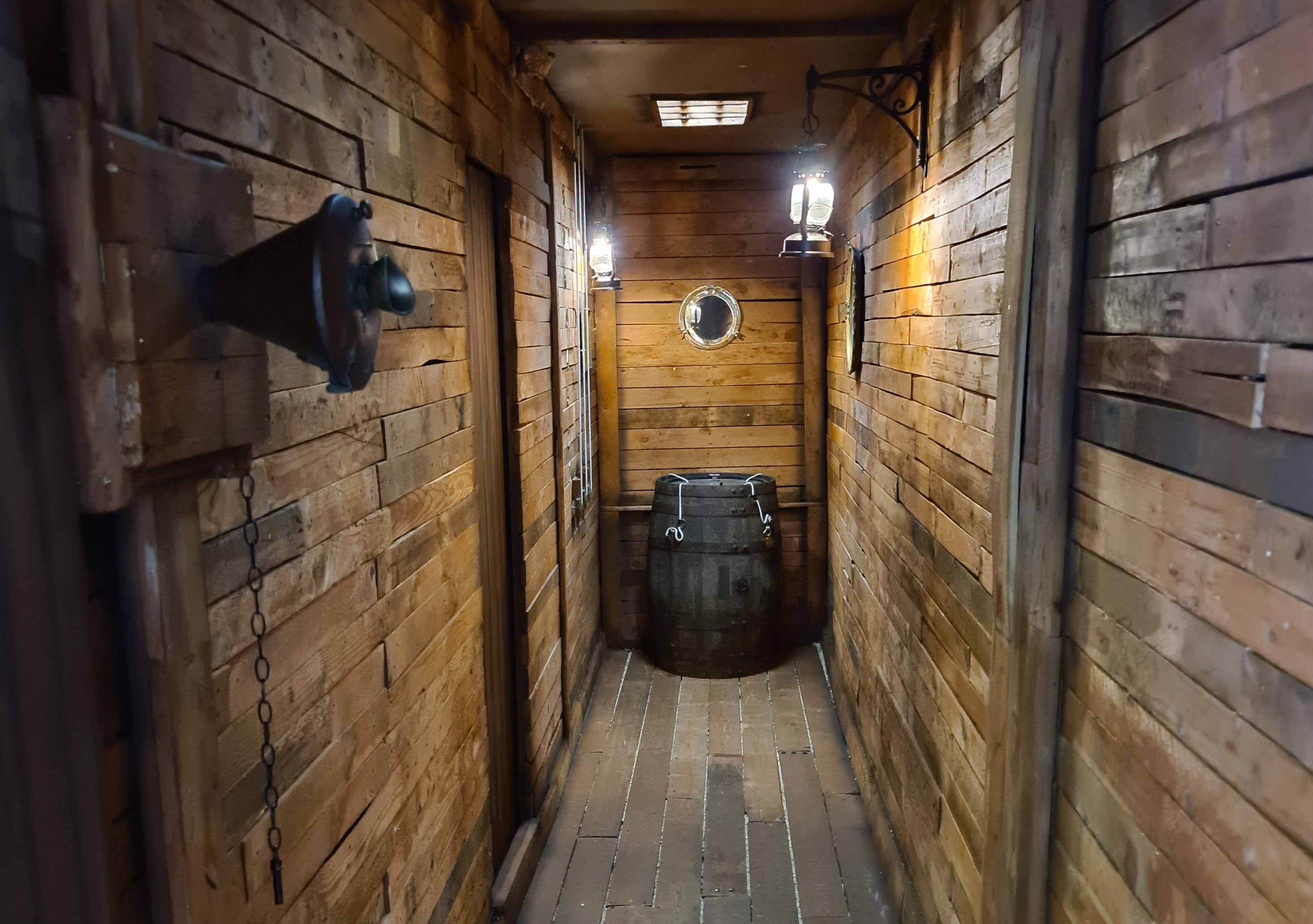 A narrow passage with wood each side. At the end you can see a woodeen barrel.