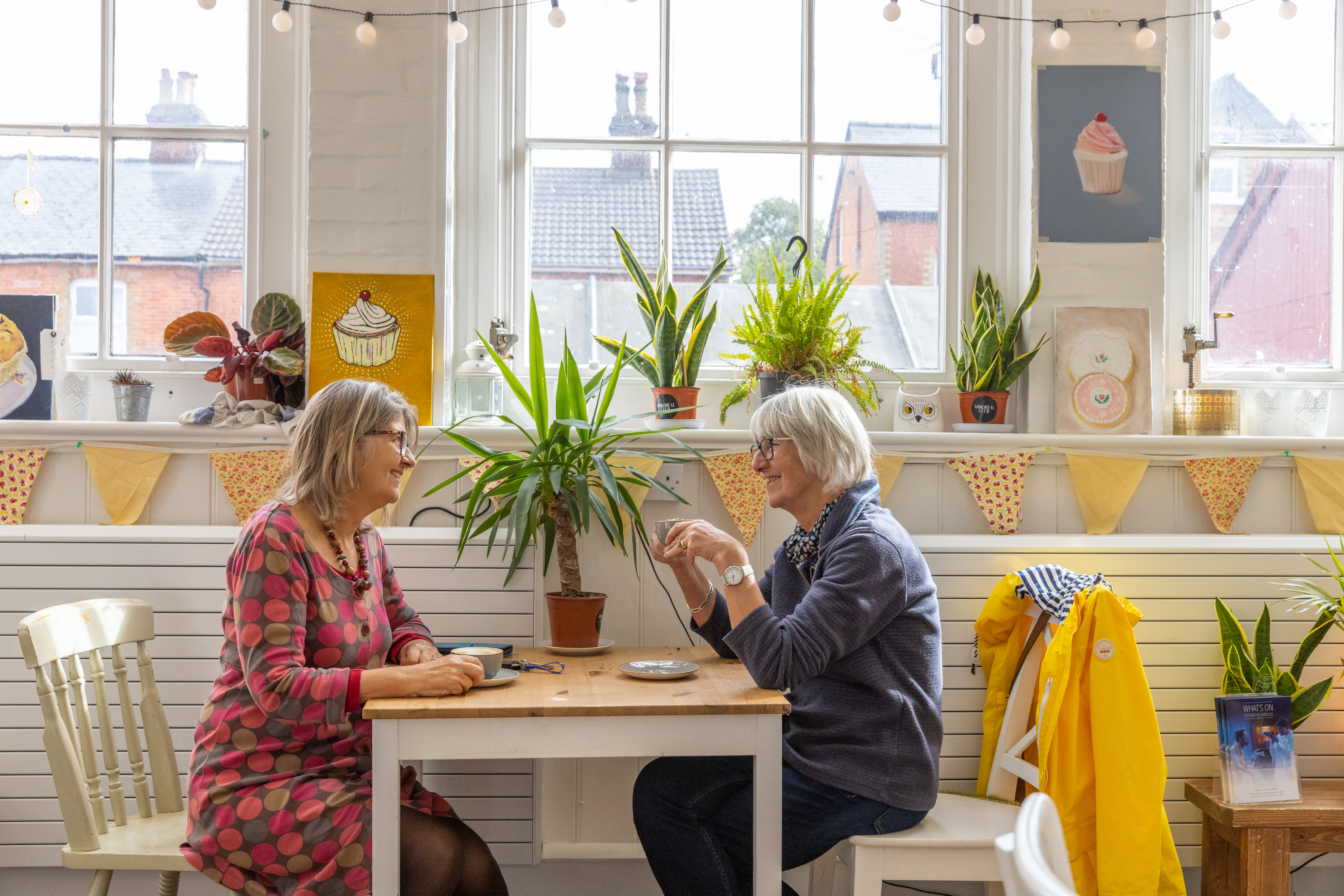 Two ladies sitting facing each other, smiling. Having a conversation over a cup of coffee.