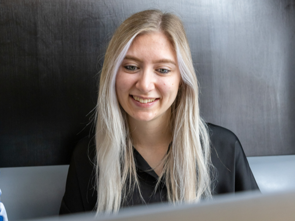 A female sits behind a laptop looking at the screen and smiling.