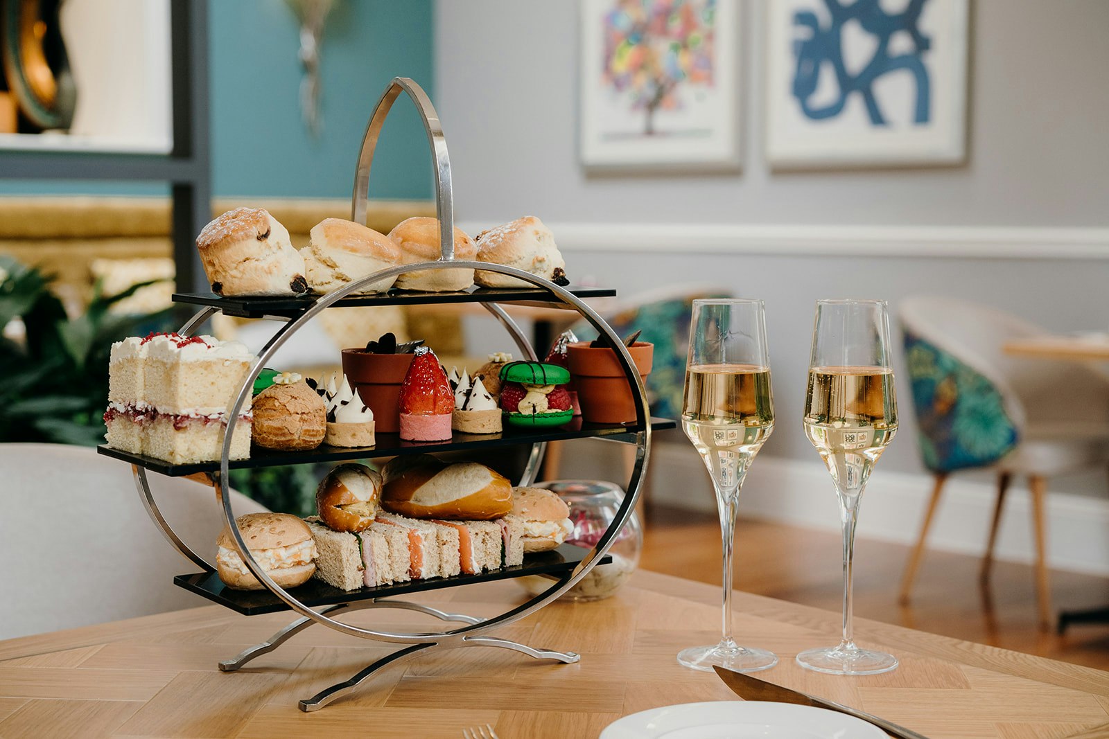 A cake stand for an afternoon tea. It is full of scones, sandwiches and cakes. There are two glasses of champange next to the stand. Oakley Hall, Basingstoke's  resturant is in the background