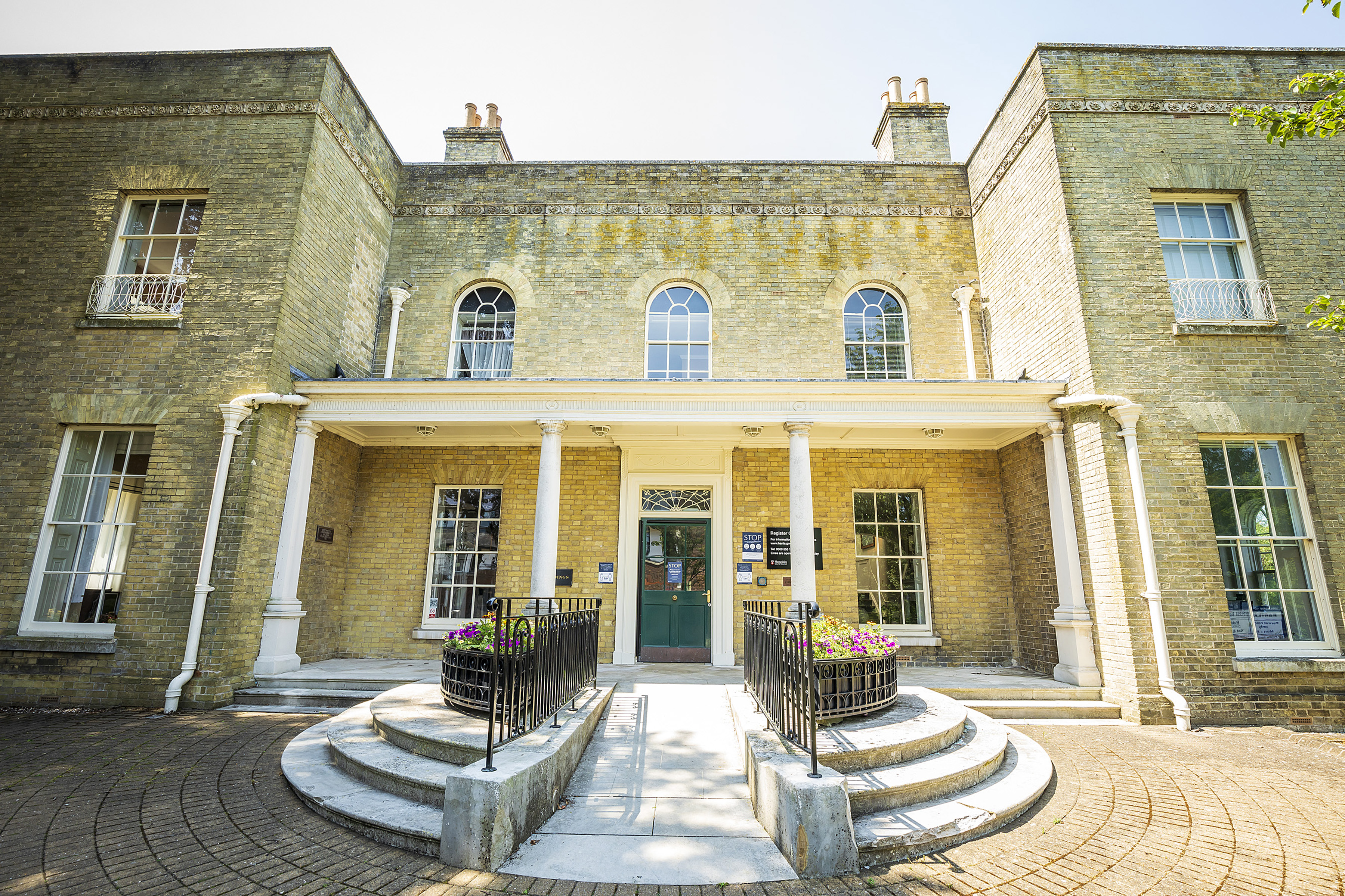 A photograph of Goldings, Basingstoke Registration Office. Ornate concrete steps and ramp lead to a green front door of this historic Georgian building.