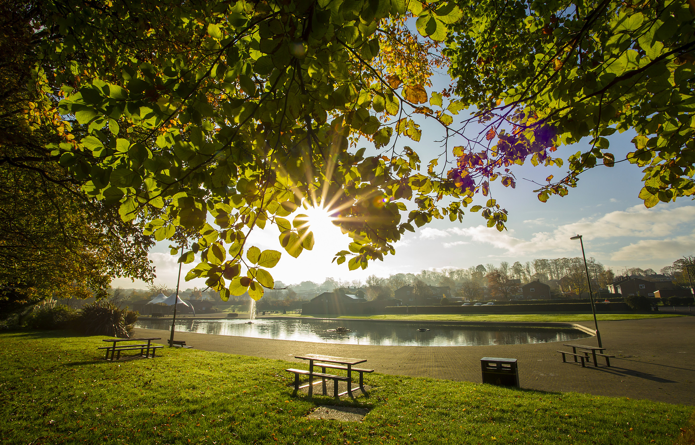 Eastrop Park, you can see a couple of benches and then the lake. The sun shines through the trees.