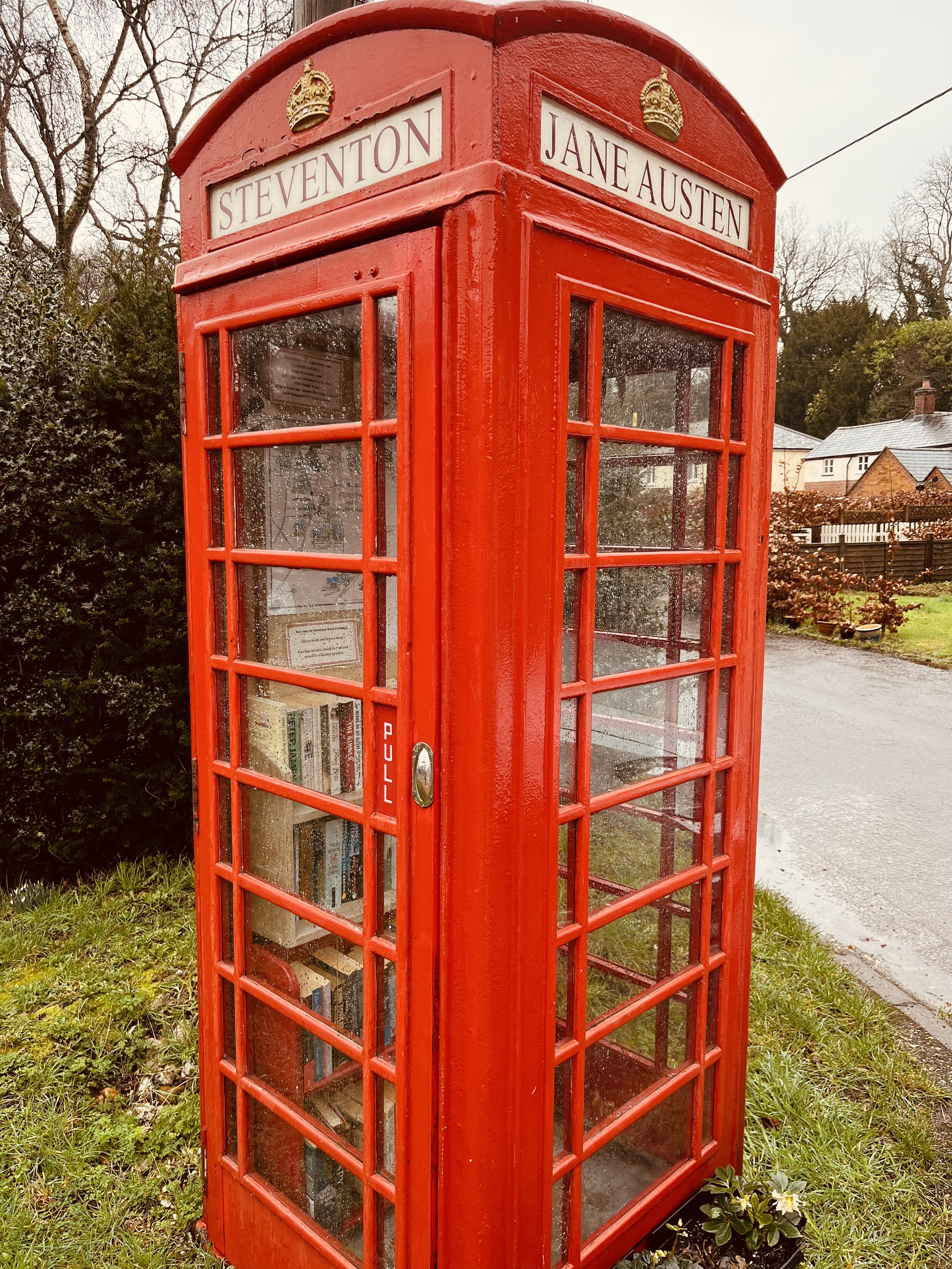 A traditional red phone booth is photographed in Steventon. The phone box has been converted into a library, books are stacked inside.