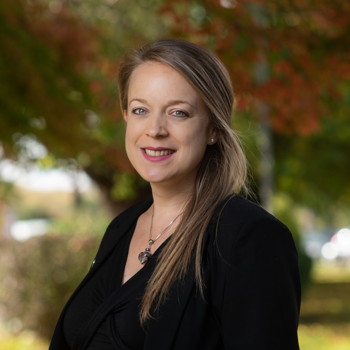 A female looks at the camera and stands in front of a blurry outside background.
