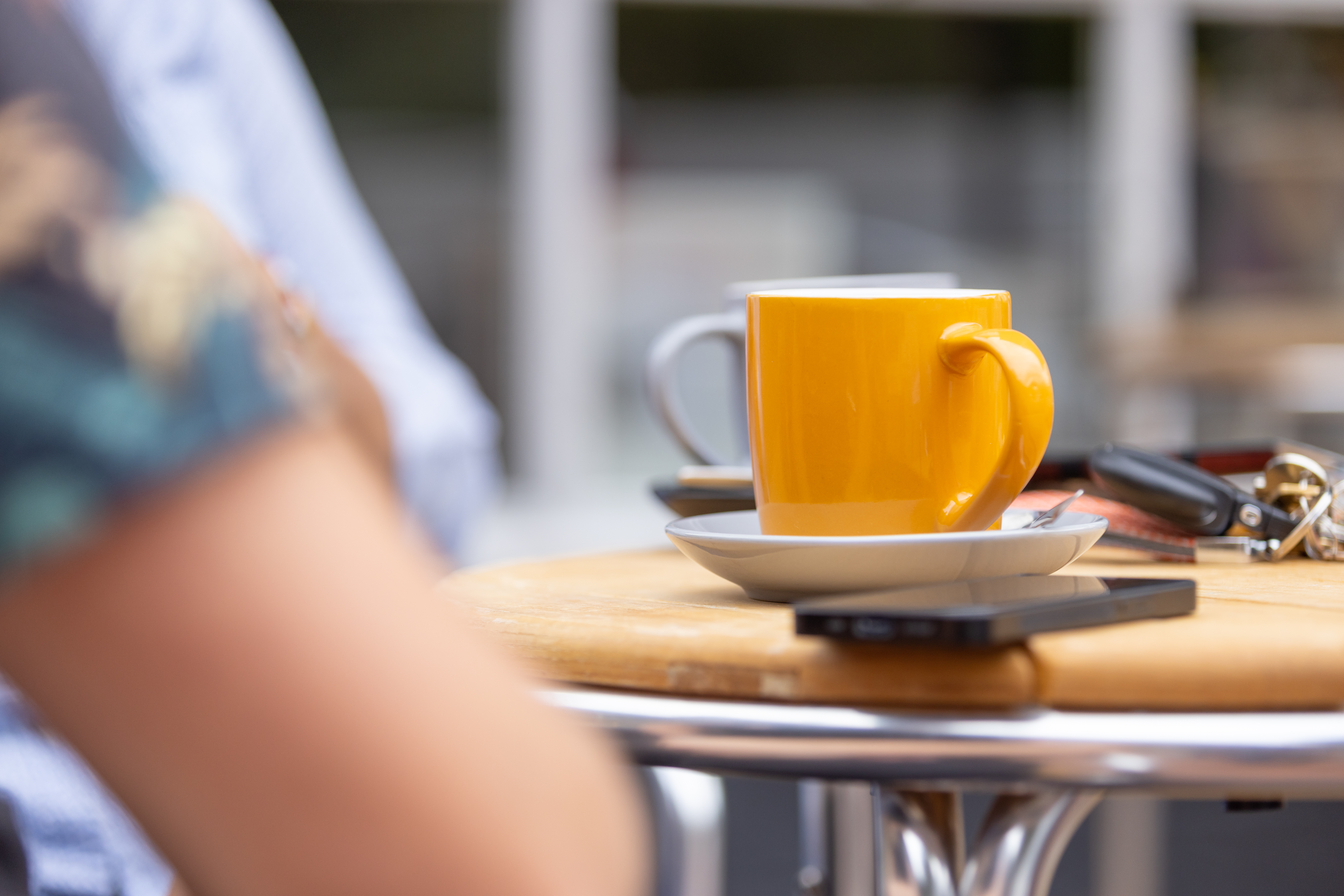 A yellow coffee cup sits on a table outside with people.