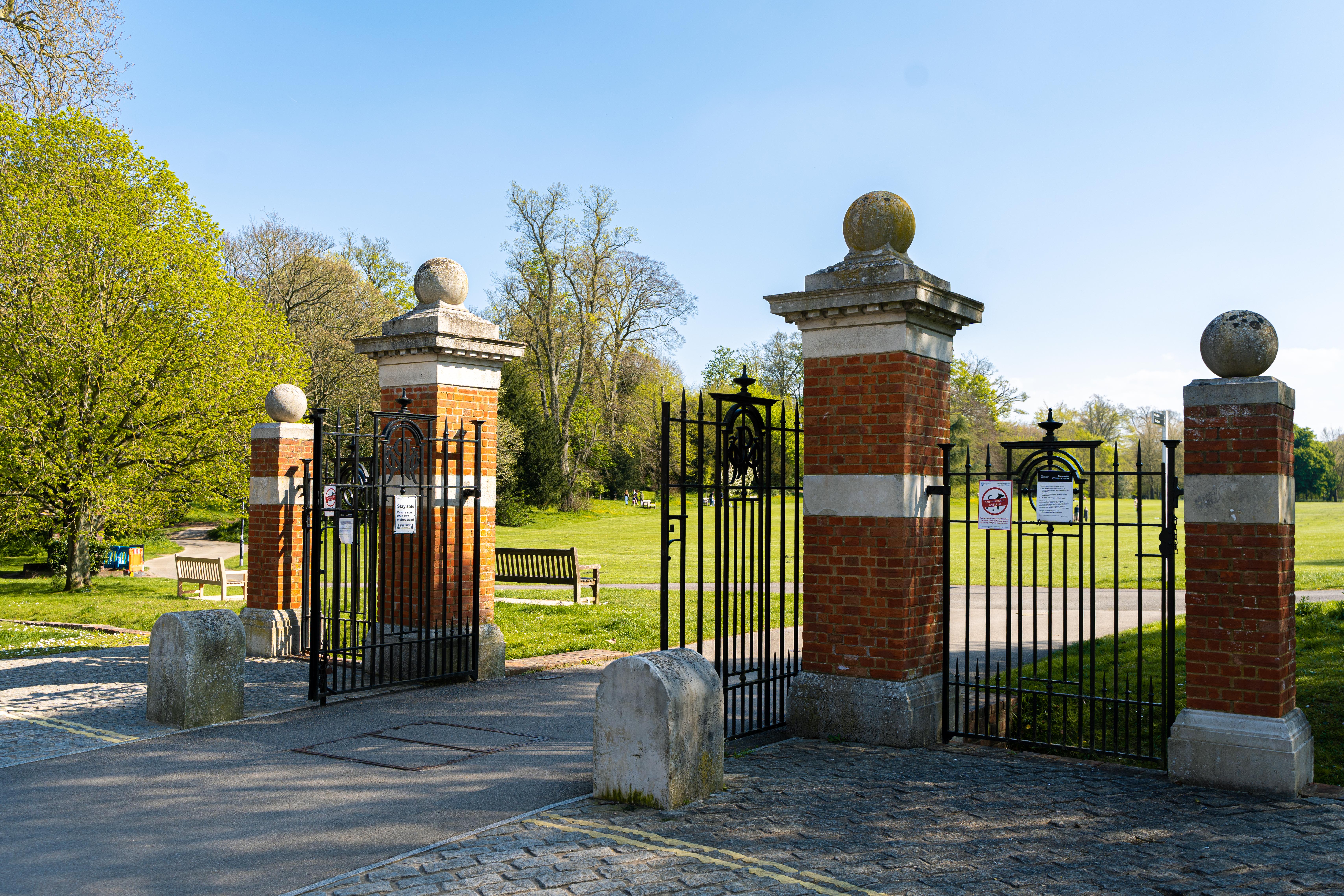 Red brick pillars with stone balls on top. Black metal gates. Behind you can see the park.