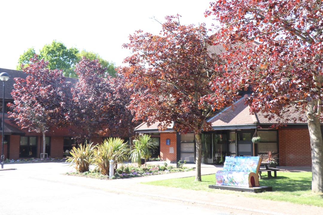 An office building with trees outside. It has some planting and a sitting with Jane bench outside.