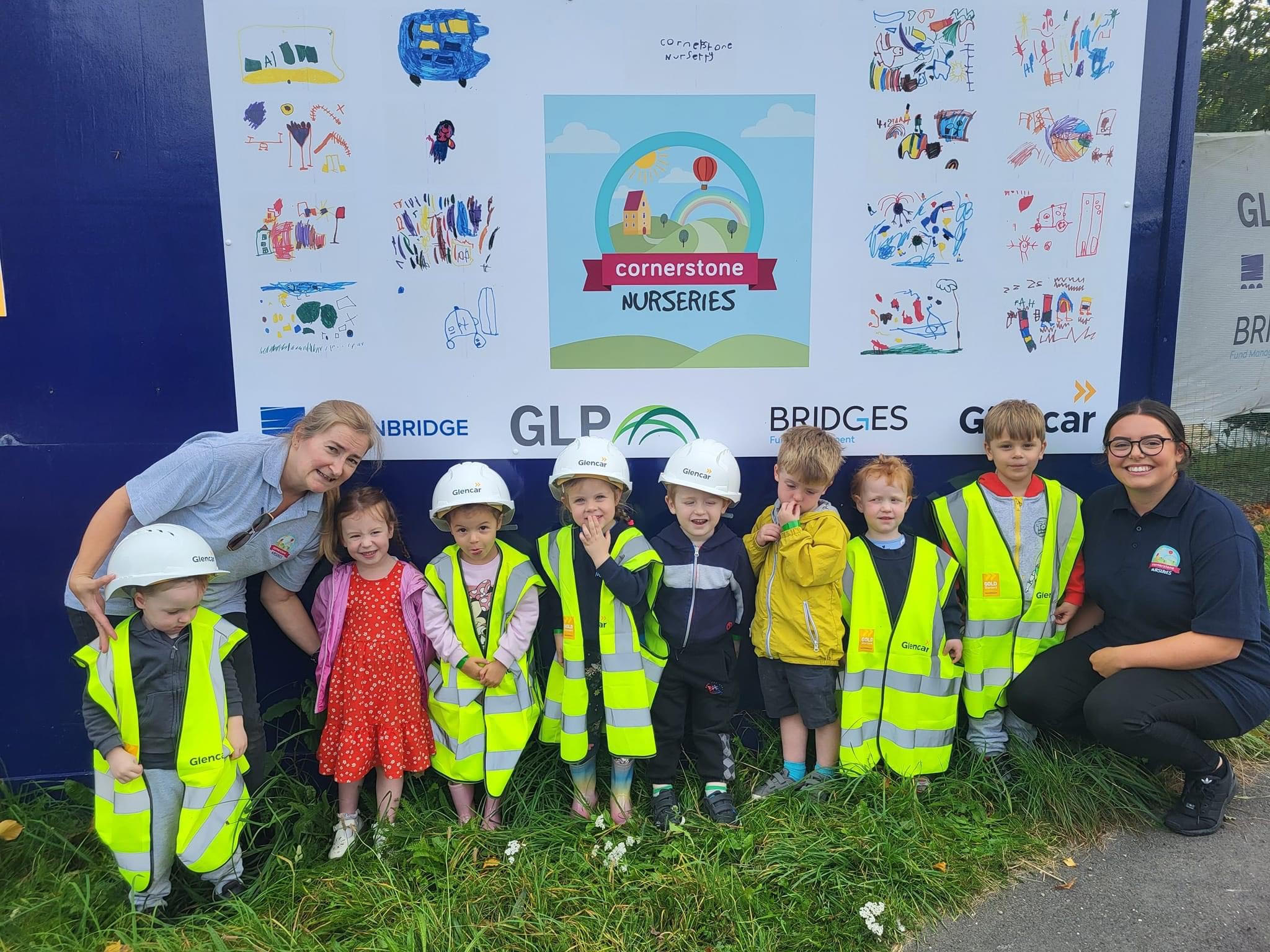A group of children wearing high viz vests standing infront of the board they designed.