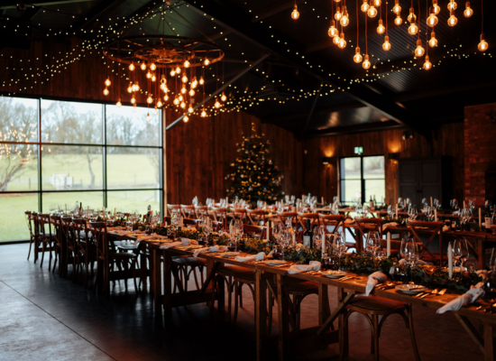 Rows of wooden tables are adorned with rustic Christmas decorations at Silchester Farm. Fairy lights hand from the ceiling.