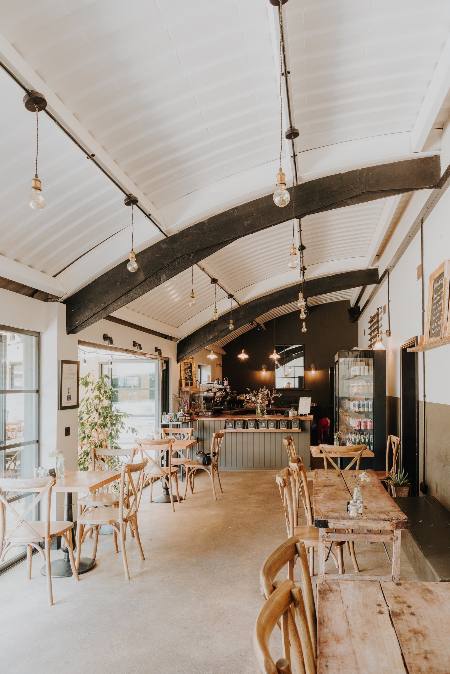 An internal photograph of The Yard in Chiltern Candover. The cafe has a curved ceiling, wooden tables and rustic chairs and decorations.