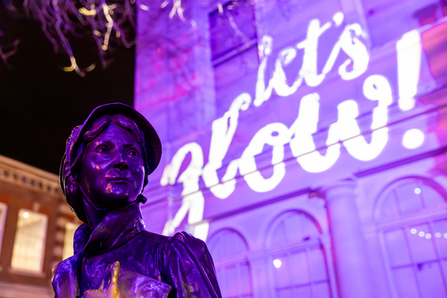 The Let's Glow logo lit onto The Willis Museum with Jane Austen's statue in front.