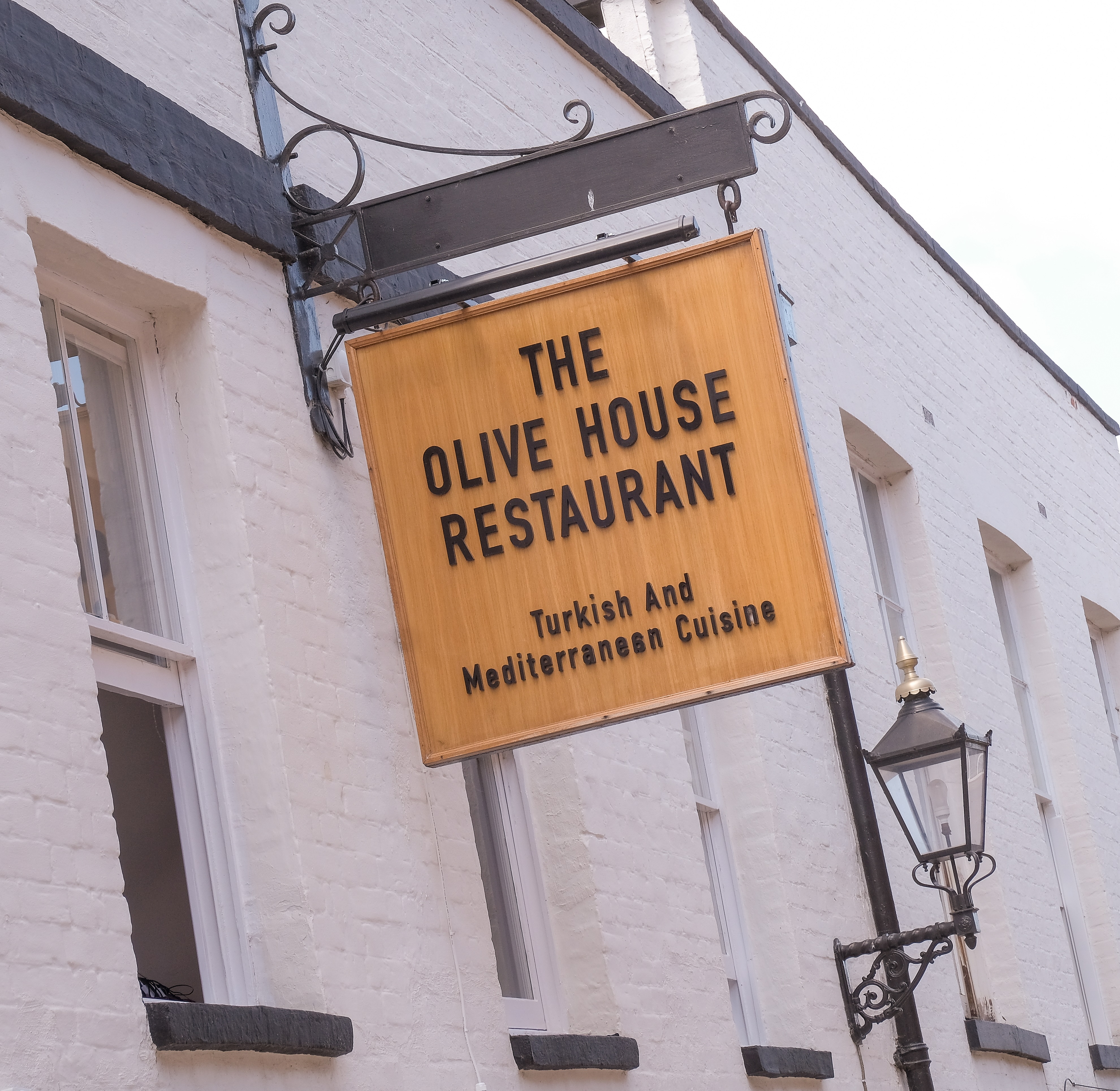 A wooden shop sign for Olive House Restuarant, attached to the front of a white building