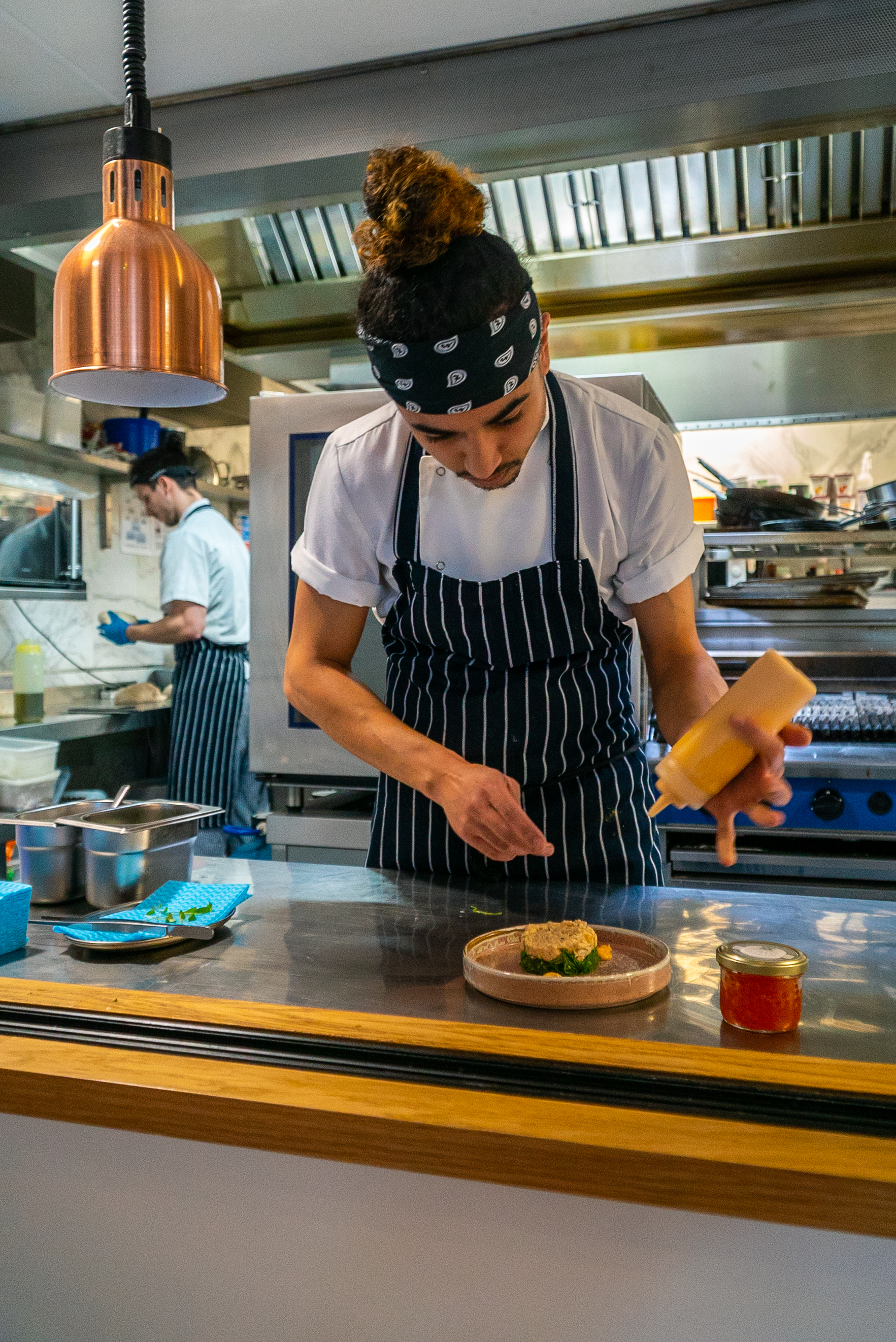A chef at The Palm Brasserie, standing in the kitchen pouring a sauce onto a dish.