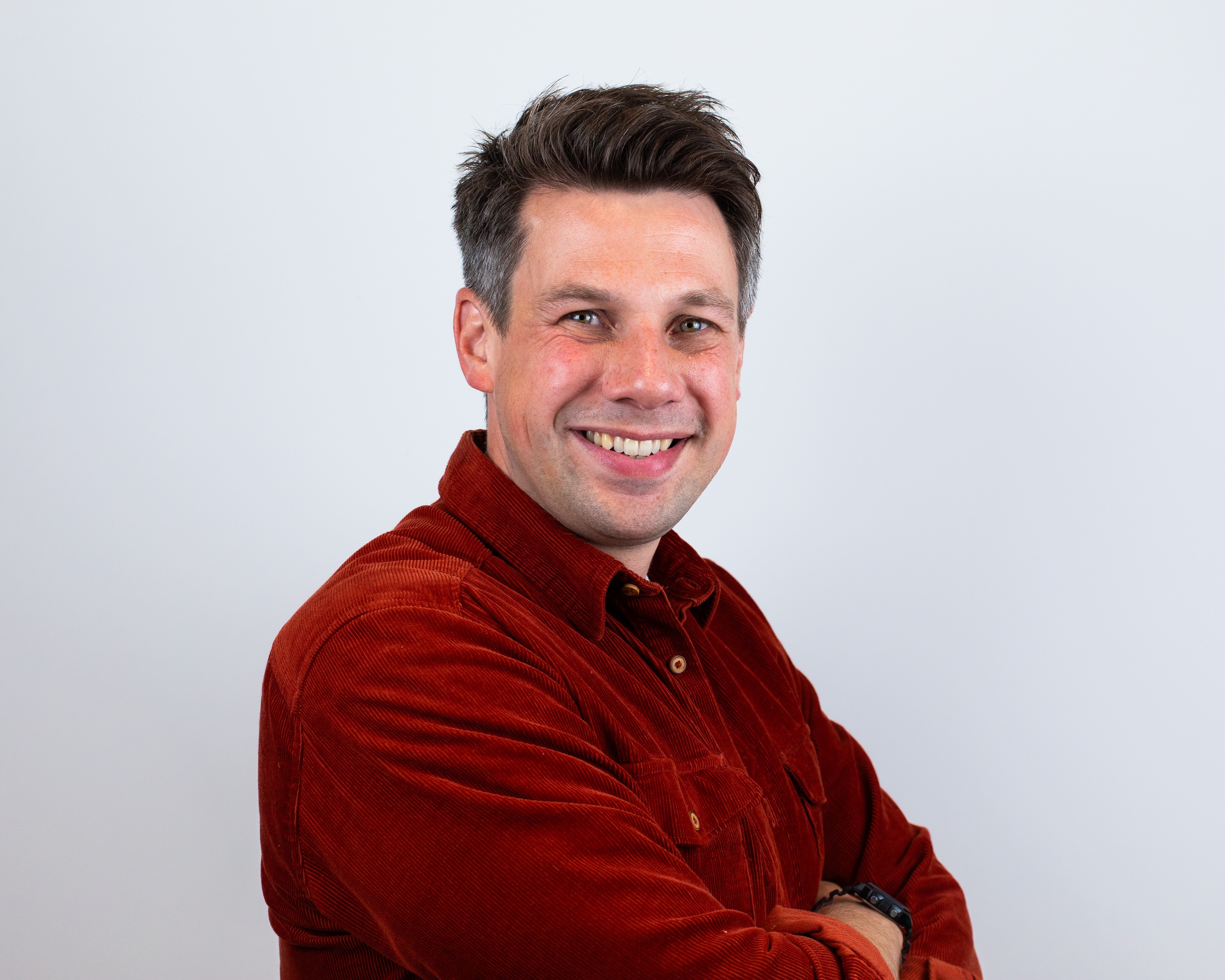 A male looks at the camera and smiles. He wears a red shirt.