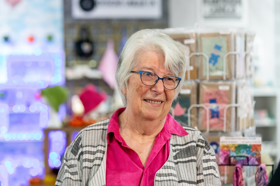 A female wearing a bright pink shirt and grey and white patterned cardigan. She is in a shop.