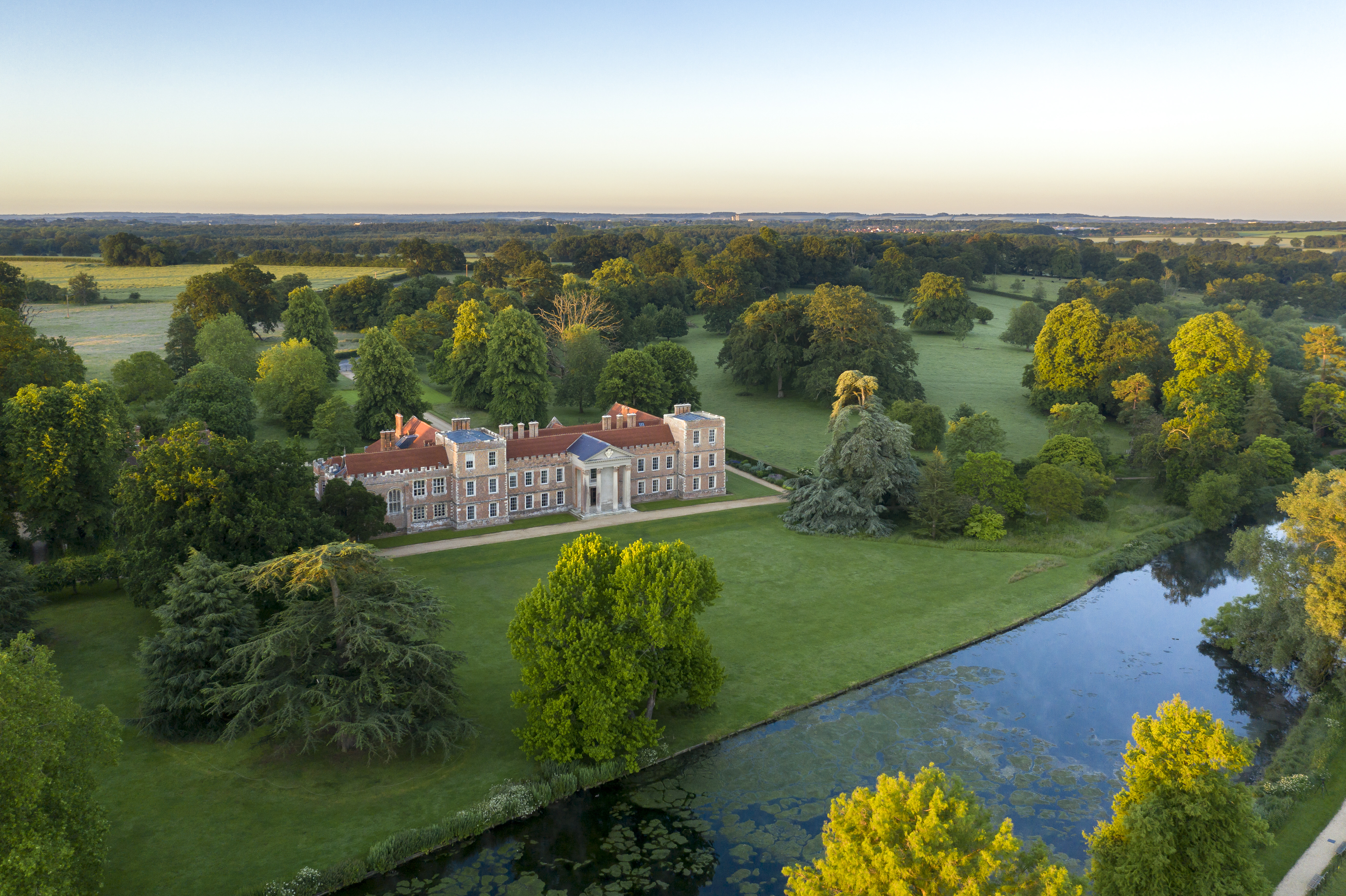 A birds eye view of The Vyne, National Trust property. A grand house nestled amoungst green trees and vast countryside. A lake runs close ot the front of the property.