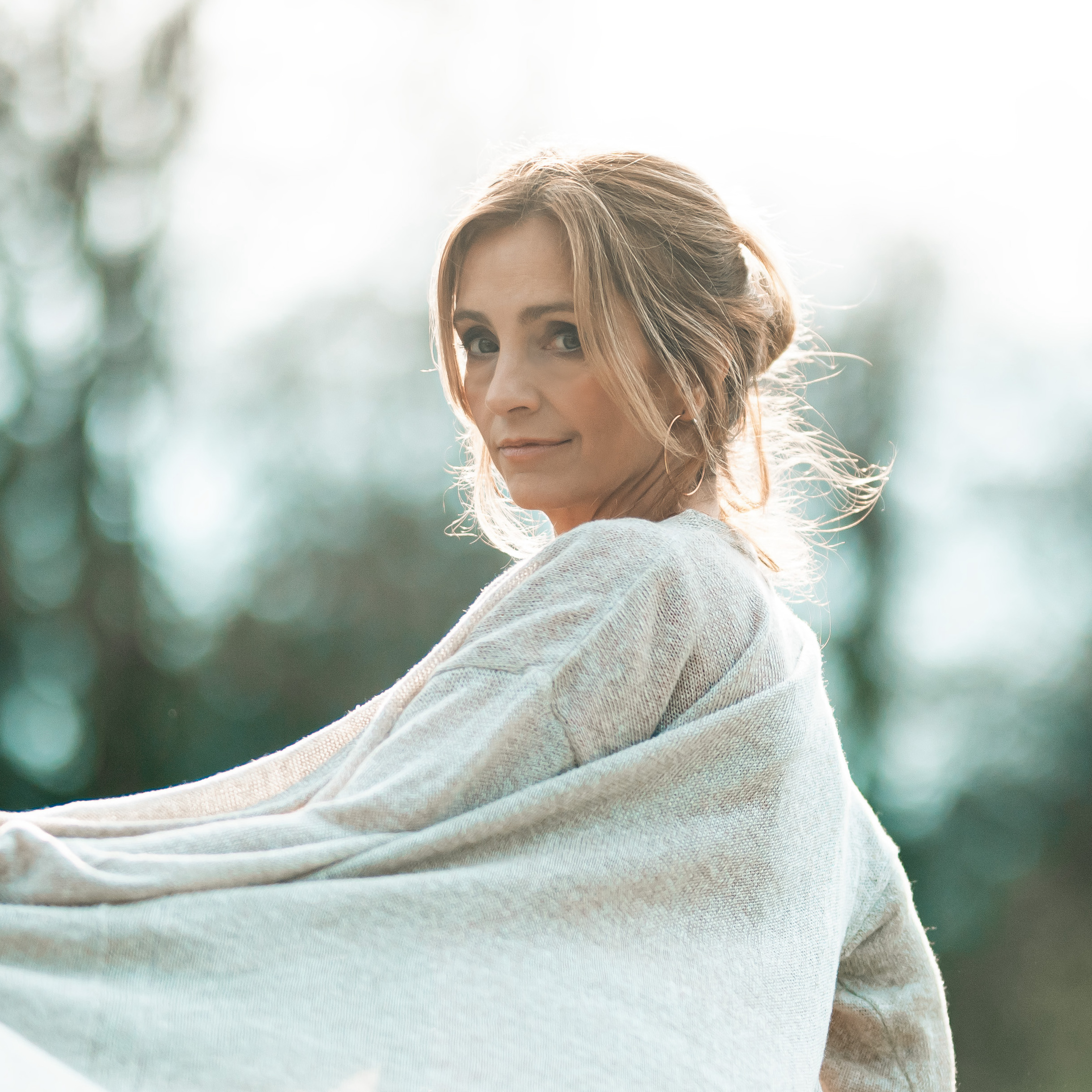 A female wears a beige jumper and is turned to the side. Her head faces forwards.
