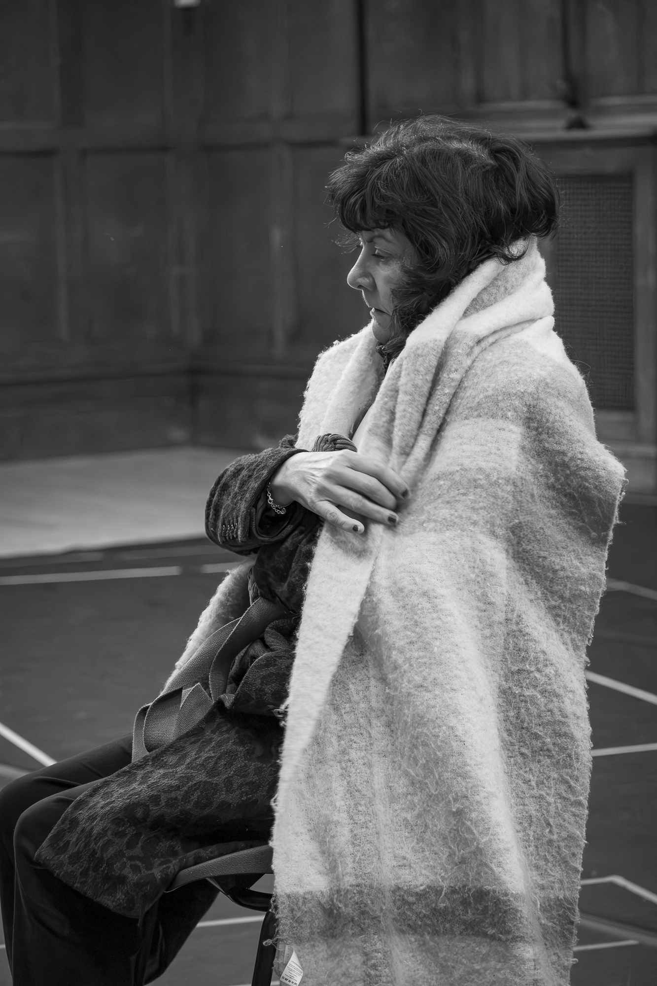 A black and white image of a female sat on a chair with a scarf around her.