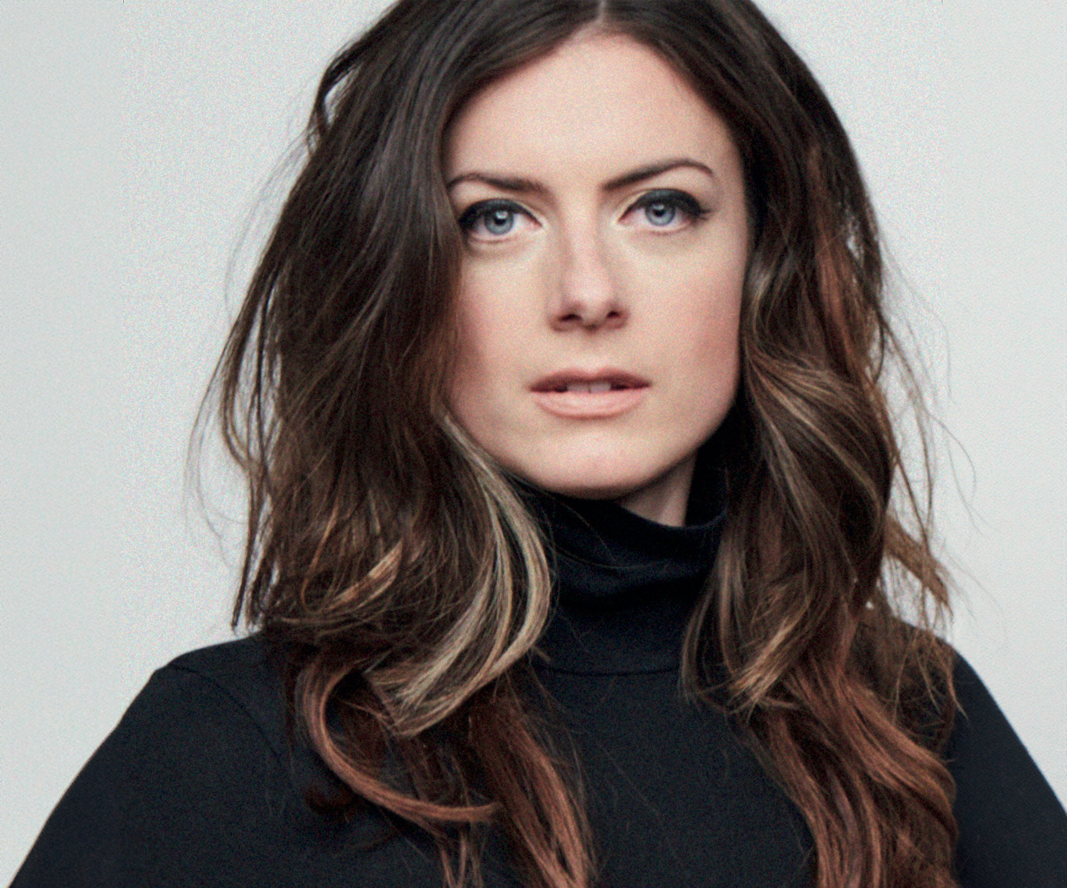 A female wears a black turtle neck and looks at the camera.